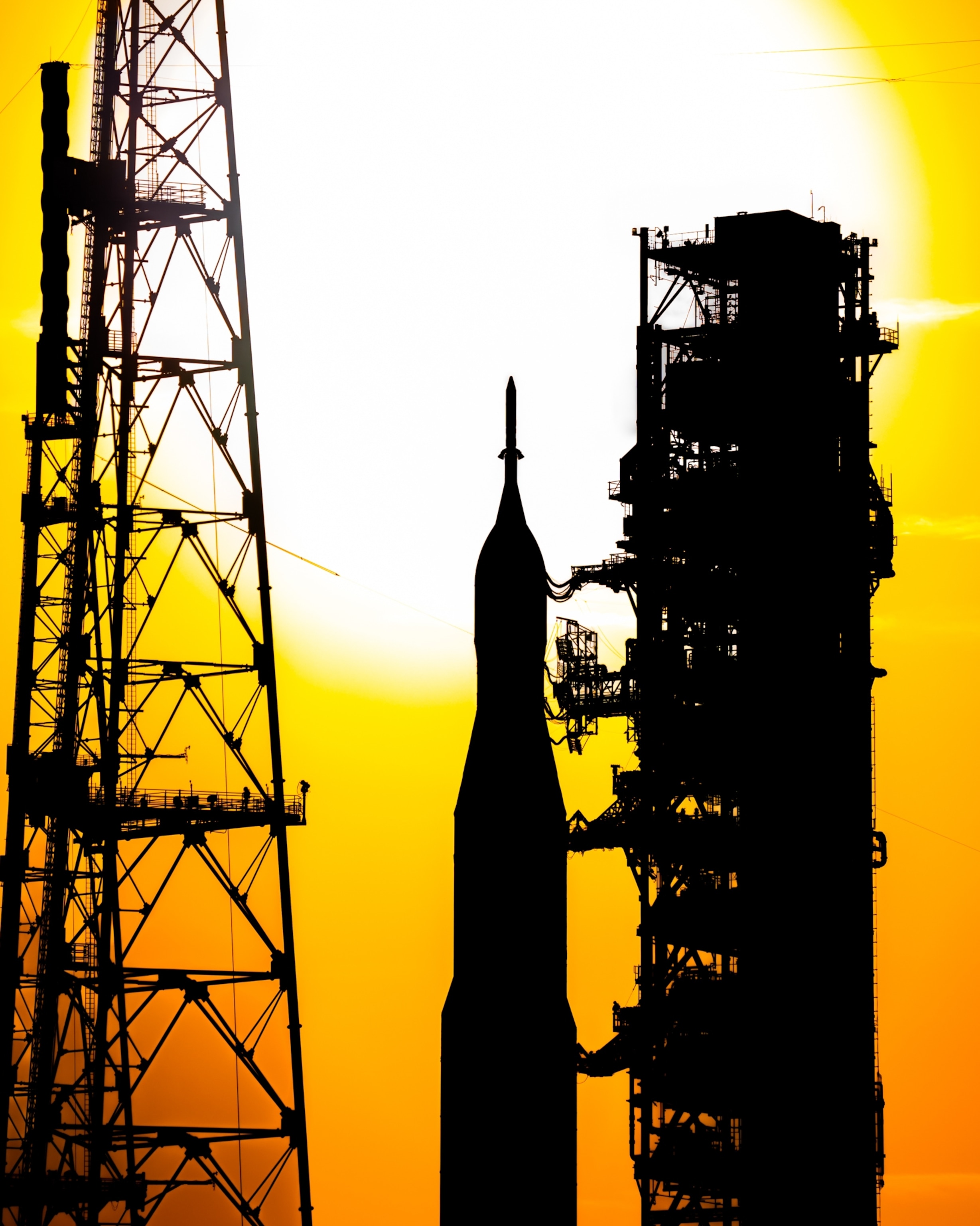 Silhouetted rocket on a launch pad against a bright, setting sun.