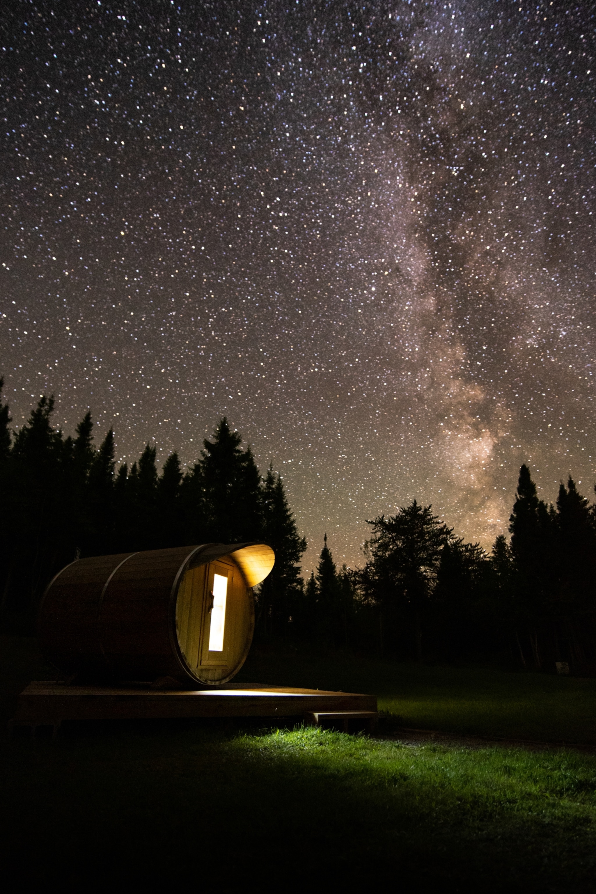 Starry night sky with the Milky Way above a barrel-shaped cabin in a forest.