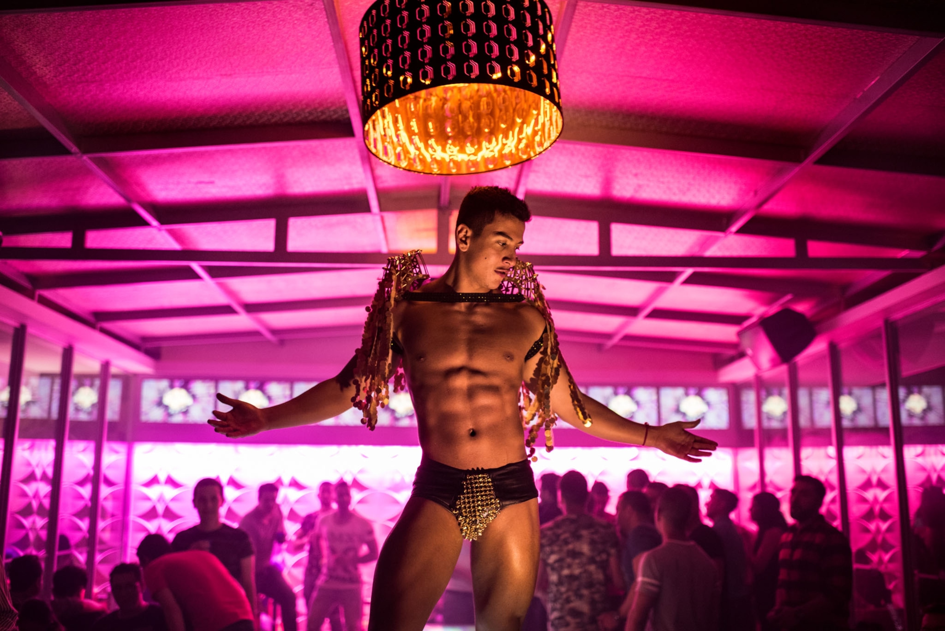 a man dancing half naked in a LGBTQ night club lit in pink lights