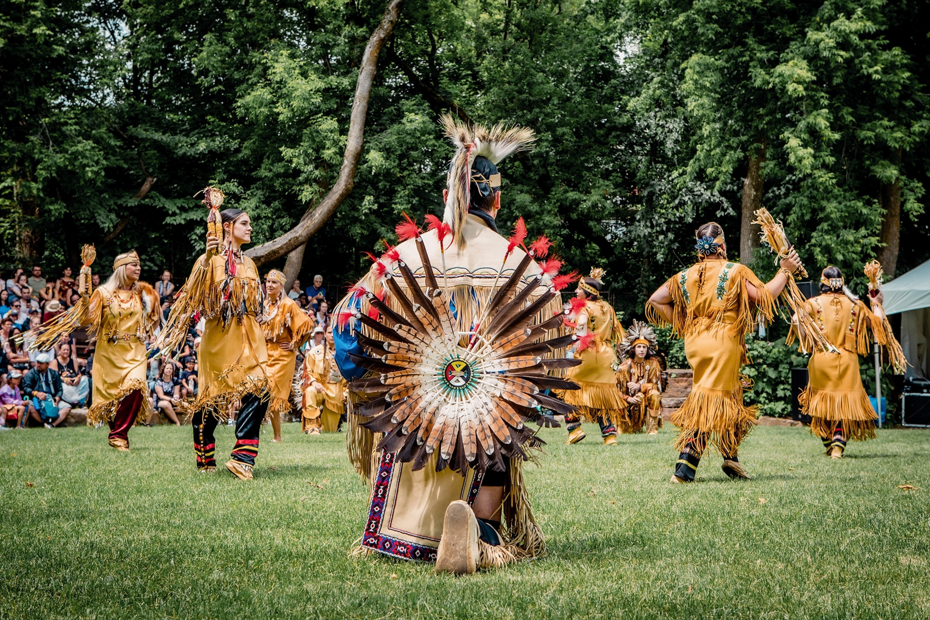 People in traditional Indigenous dress perform at an outdoor festival.
