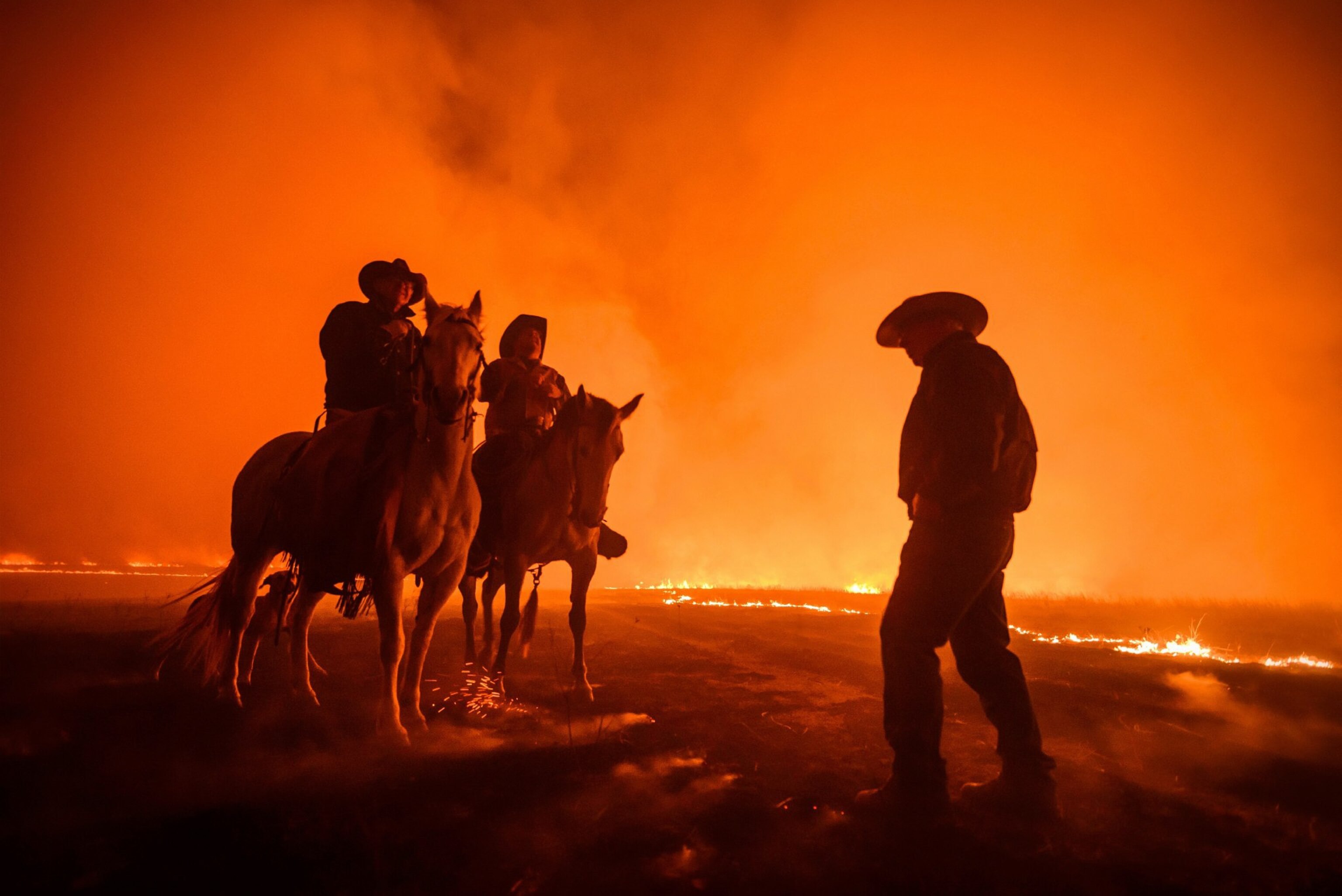 ranchers on horseback watching as the prairie burns behind them, Kansas