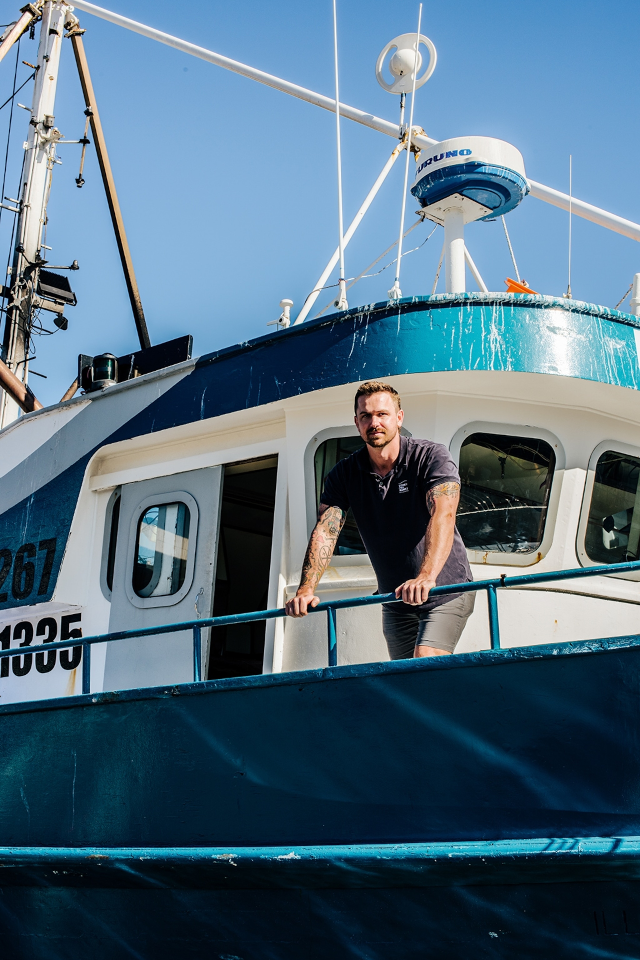 A smiling man leaning over the railing of a fishing boat with his arms stretched.