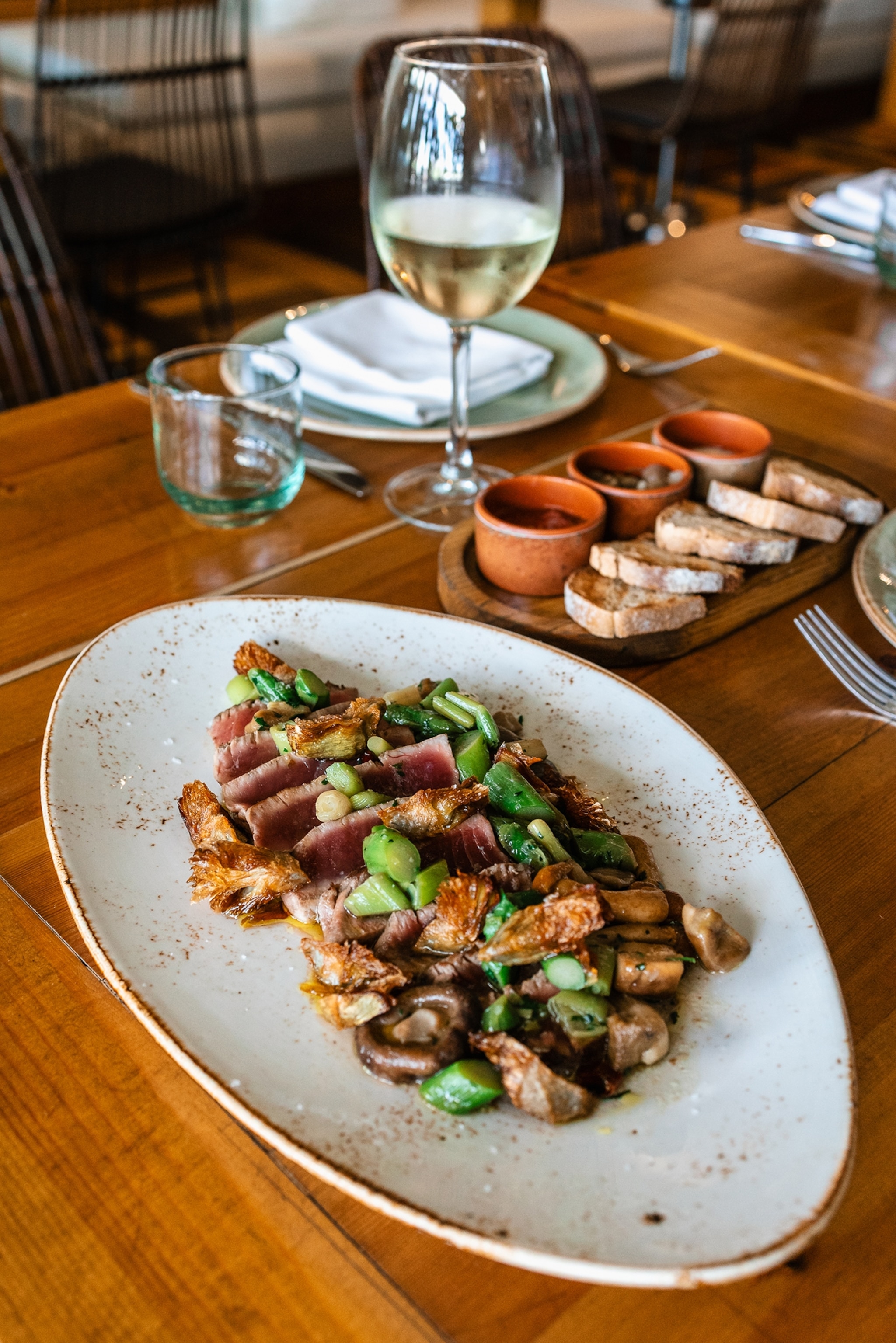 TUNA TATAKI: Seared slices of red tuna paired with mushrooms, tender garlic, and artichokes. A delicate tataki of red tuna, lightly seared to preserve its freshness and depth of flavor. Accompanied by sautéed mushrooms, sweet garlic, and artichokes slowly cooked in olive oil to maintain their essence.
