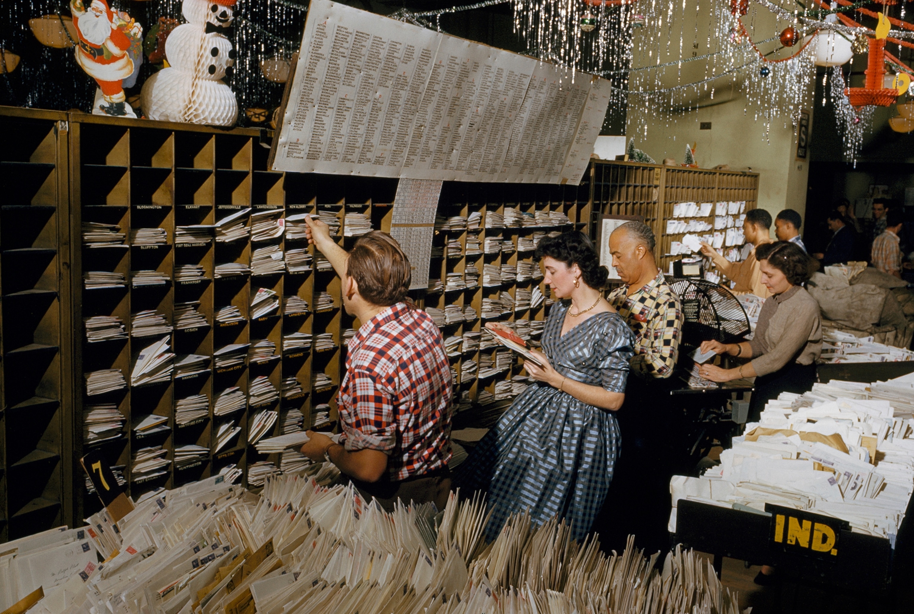 Postal clerks sort Christmas mail into slots for each destination.