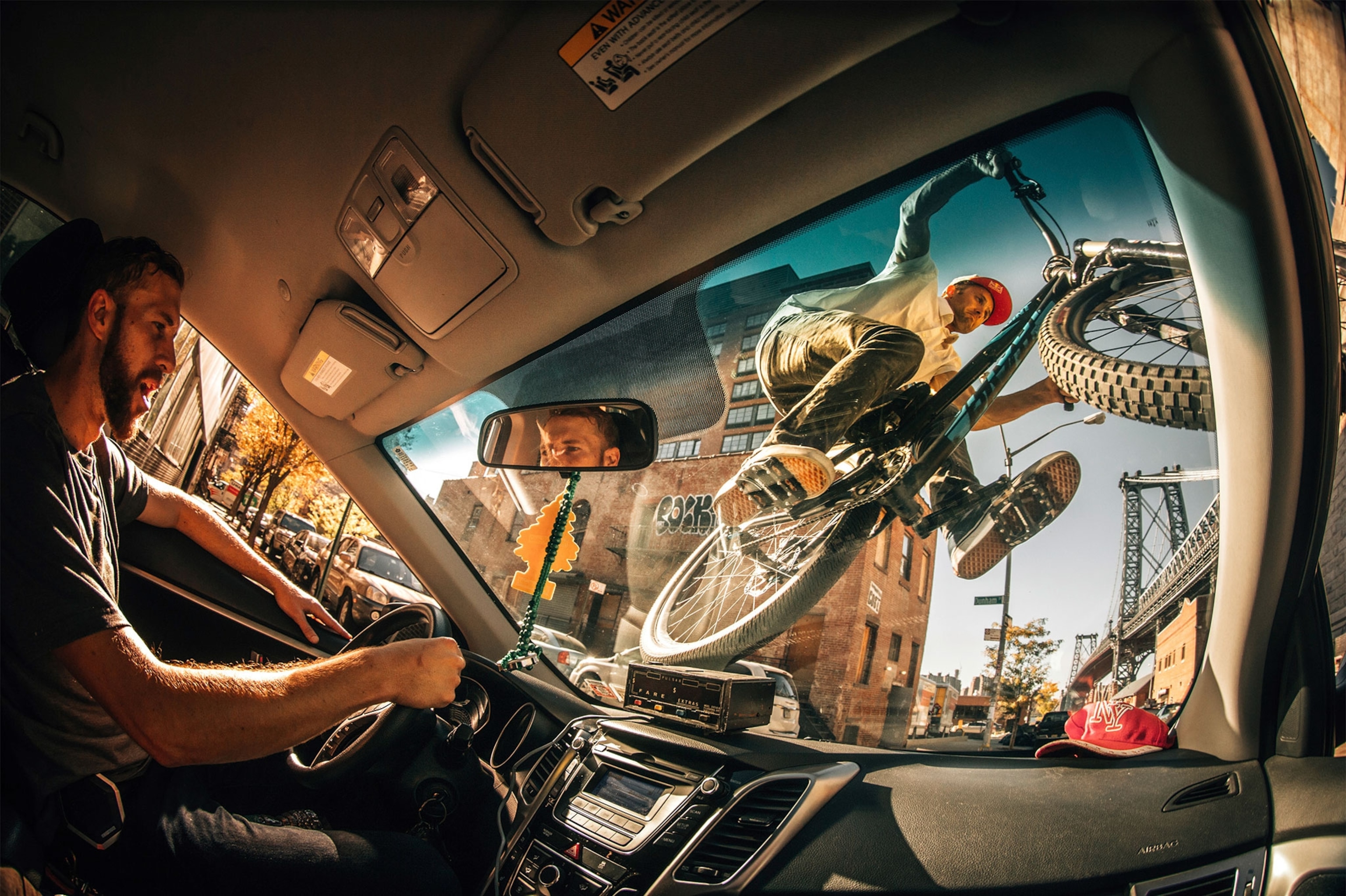 a bicyclist riding his bike over the front window of a taxi in New York City