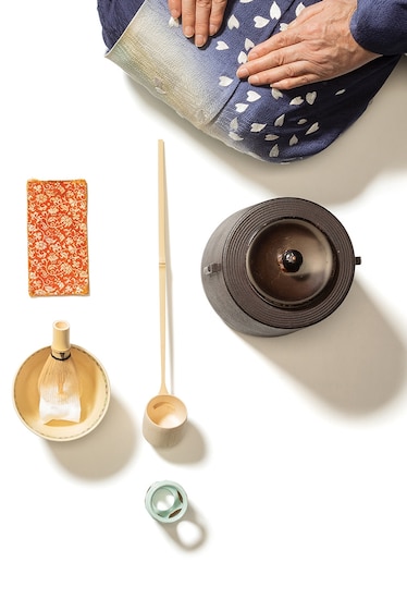Picture of tea ceremony set of dishes and utensils and woman's hands resting on laps.