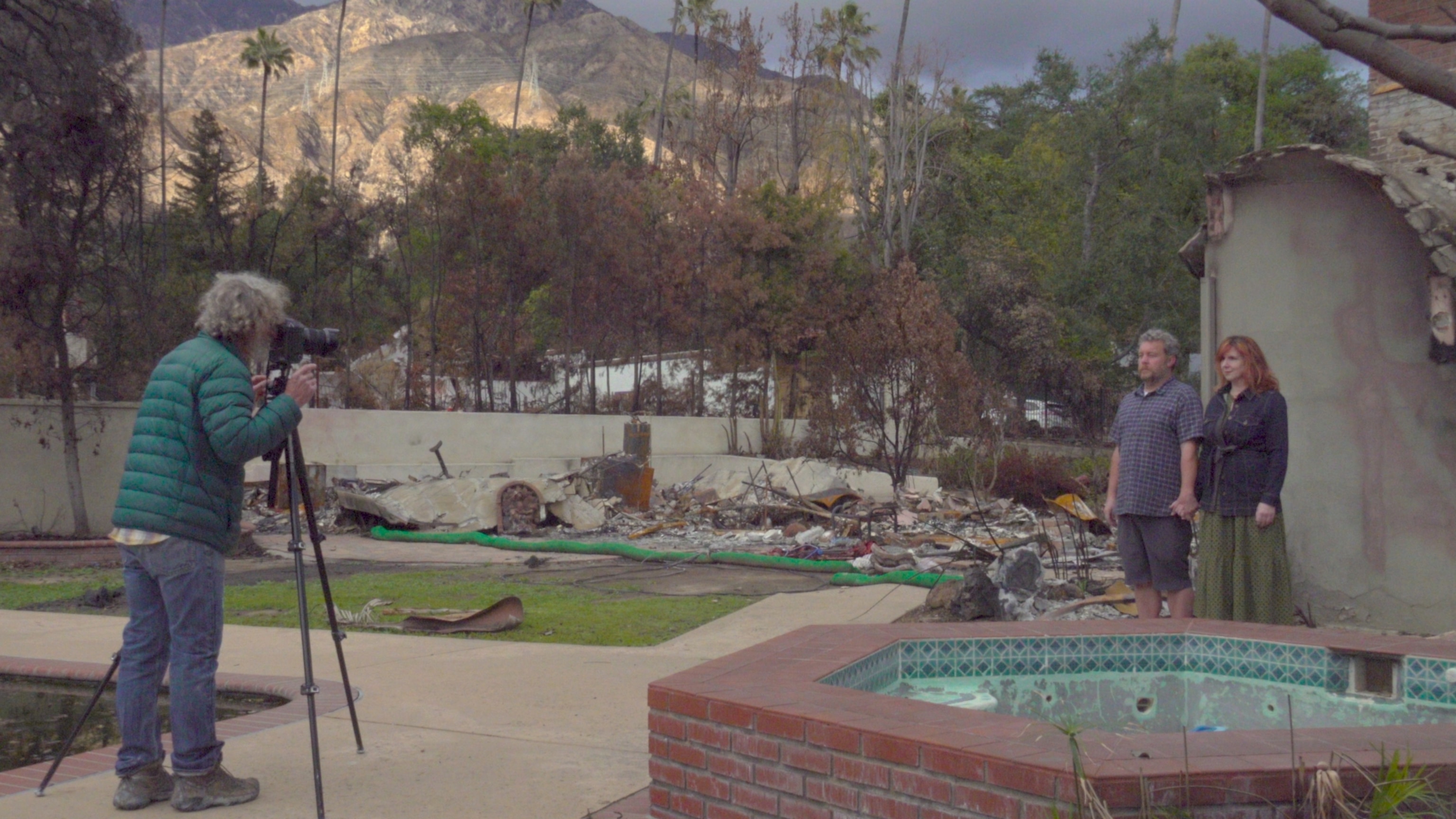 A photographer stands with a camera on a tripod facing 2 people side by side