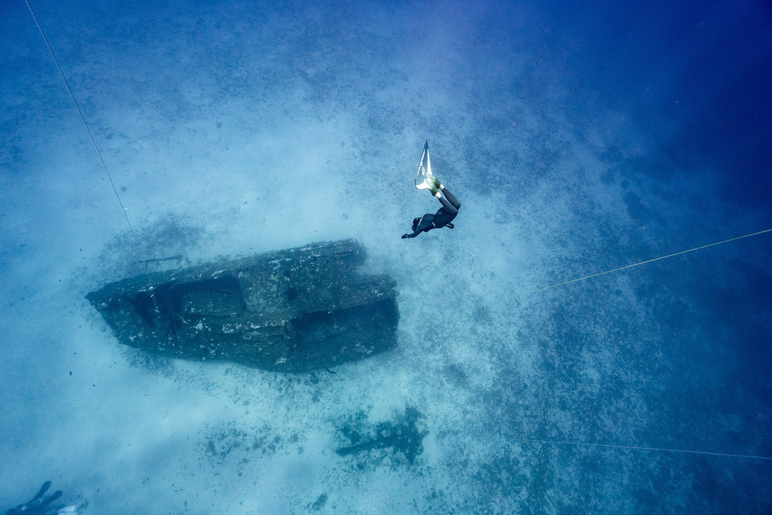A ship wreck sits in sand as a diver approaches from above.