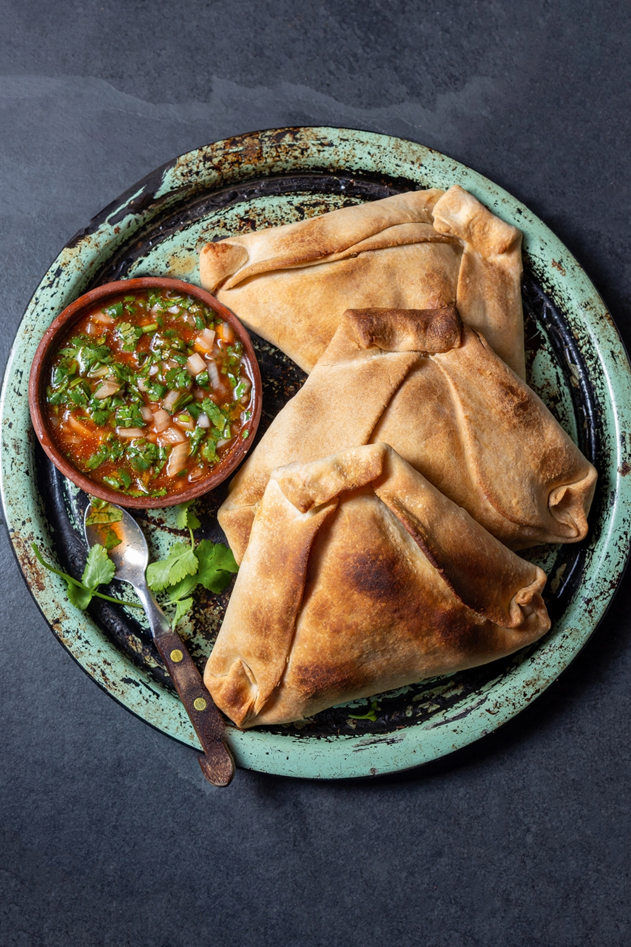 A close-up of empanadas on a plate with a spicy herb salsa on the side.