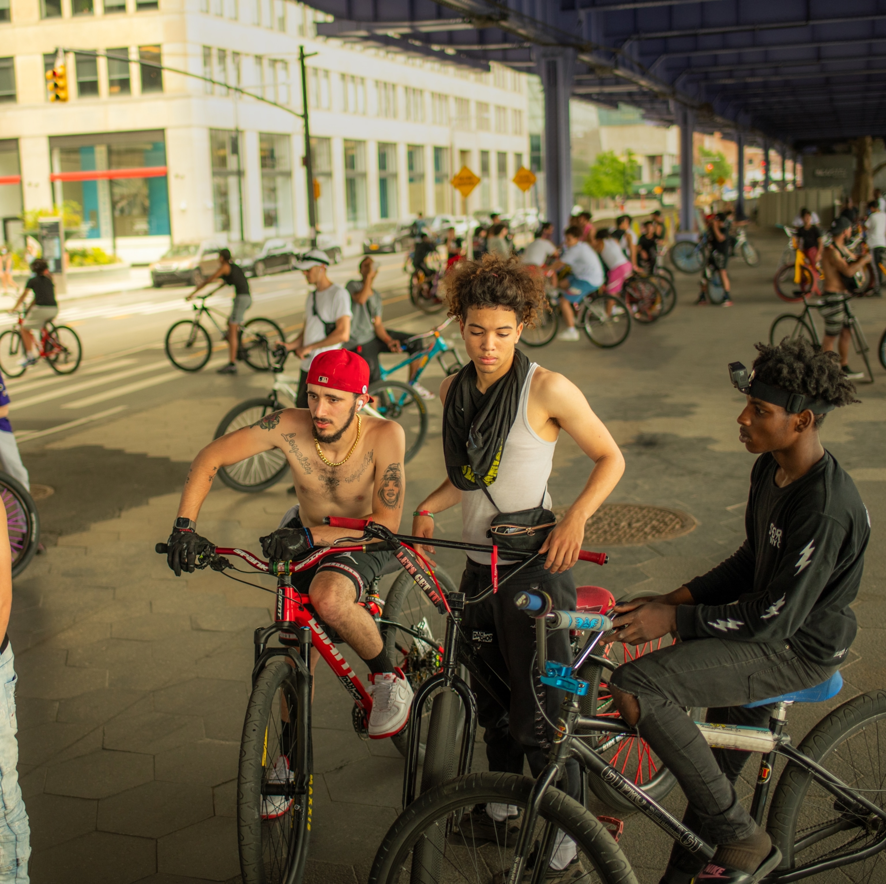 Three young men with bikes on the foreground and many bikes on the background under the pridge.