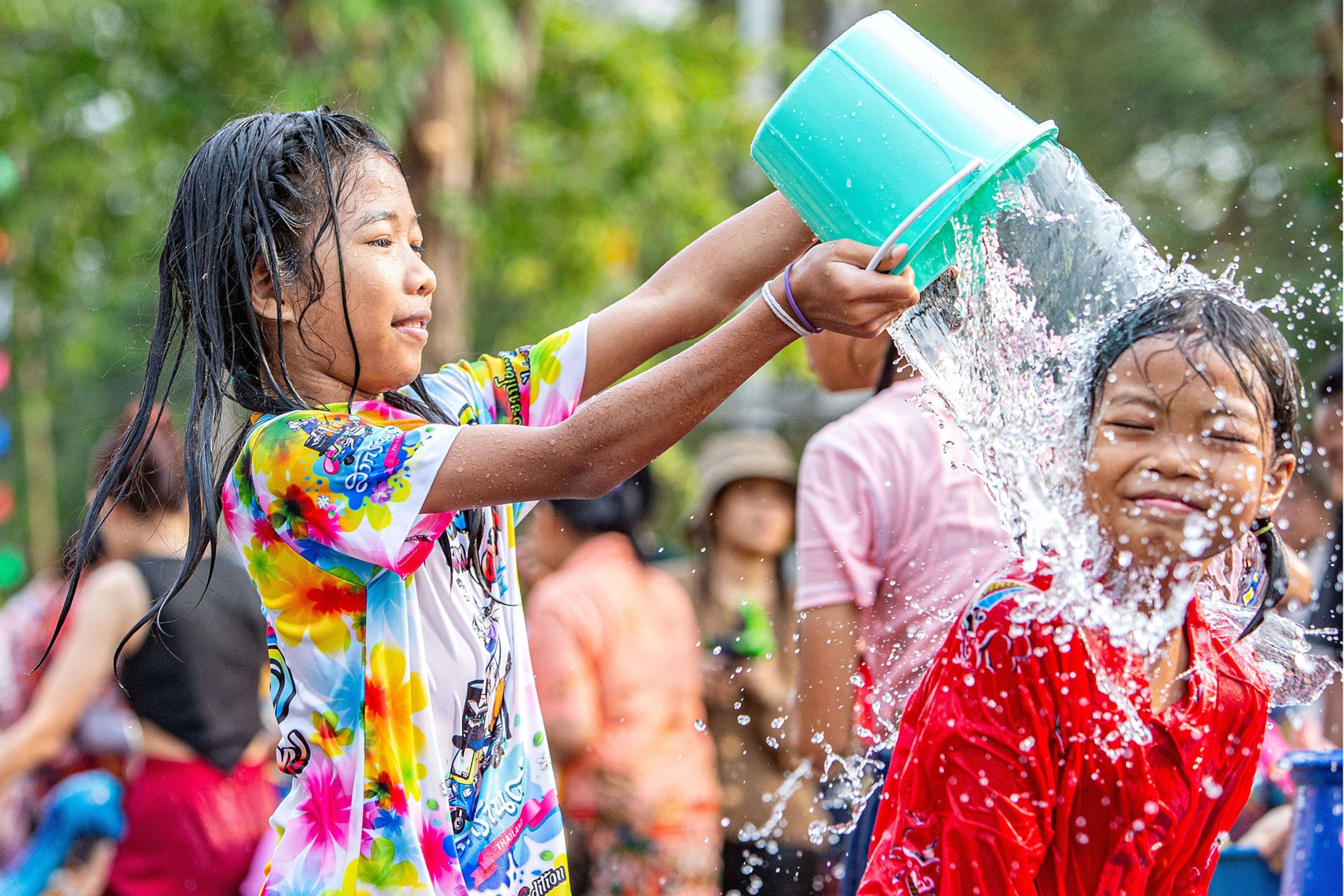 A child in wet clothes dumps a bucket of water on another smiling child's head