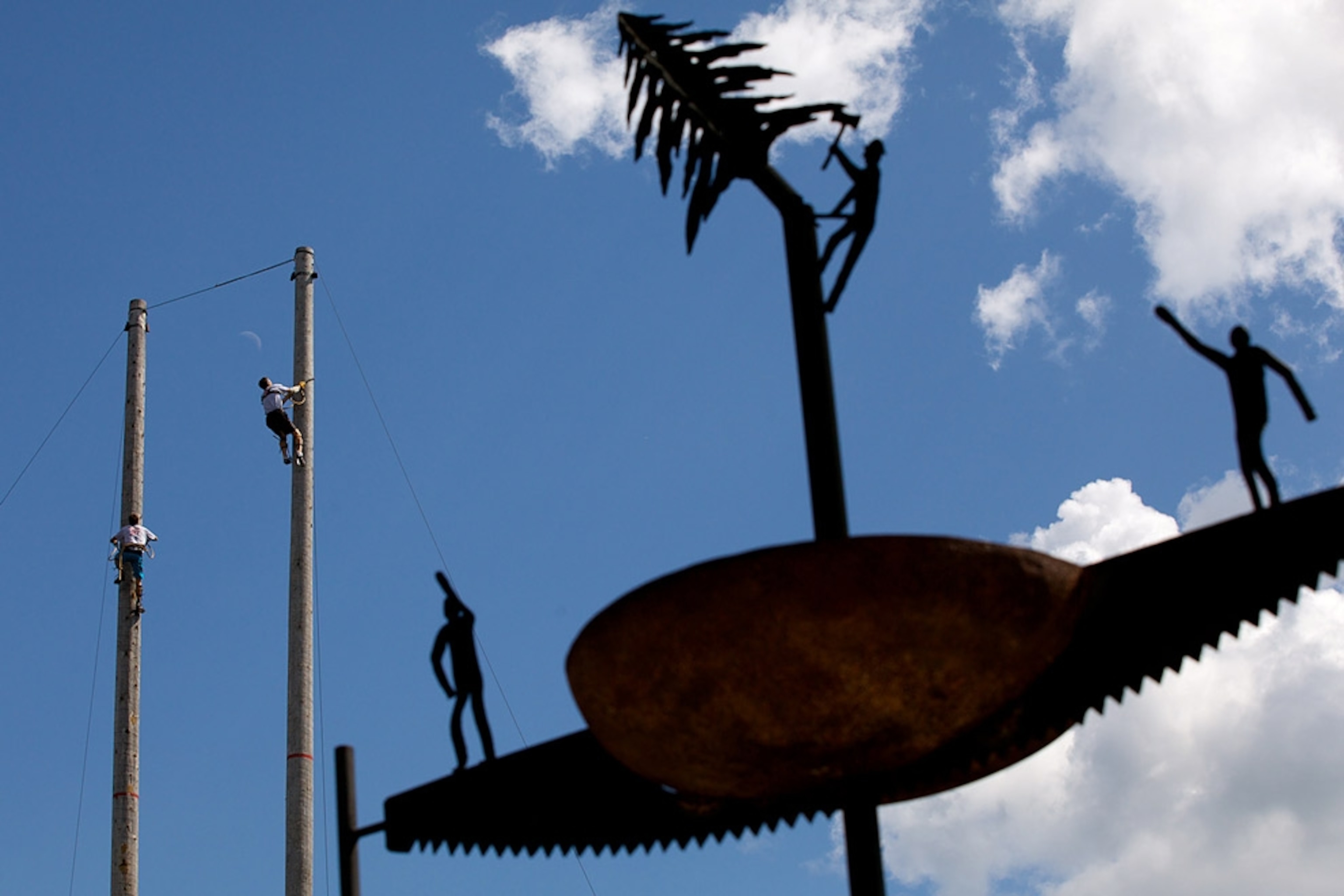 Men climbing poles behind metal sculpture
