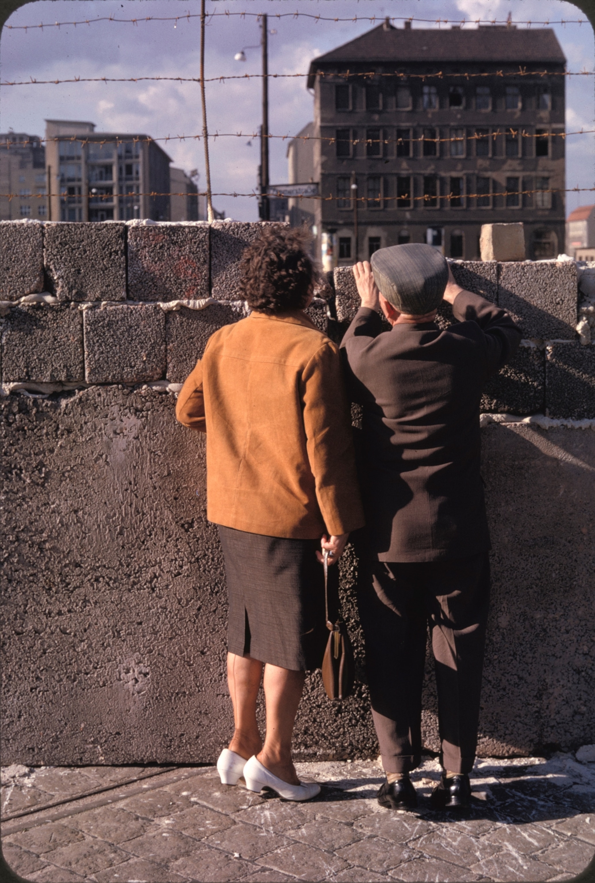Standing on tiptoe near Friedrichstrasse, West Berliners try to glimpse a relative beyond the wall. Processed rubble forms the blocks. Daring Germans have escaped by crashing through such barricades in trucks.
