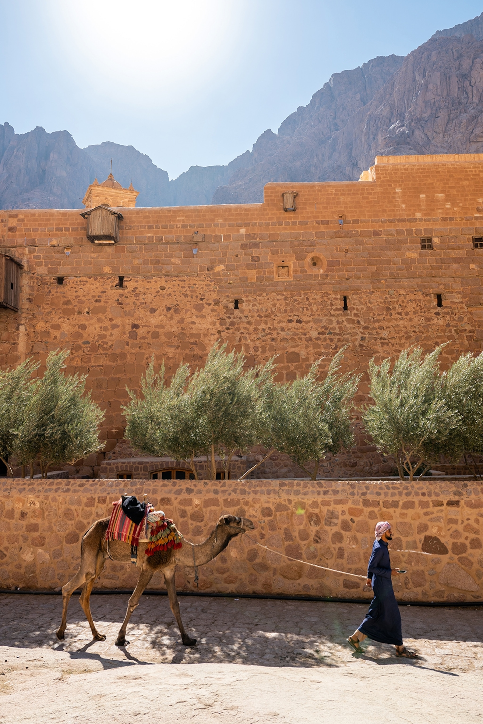 A man and his camel walk by a monastery.