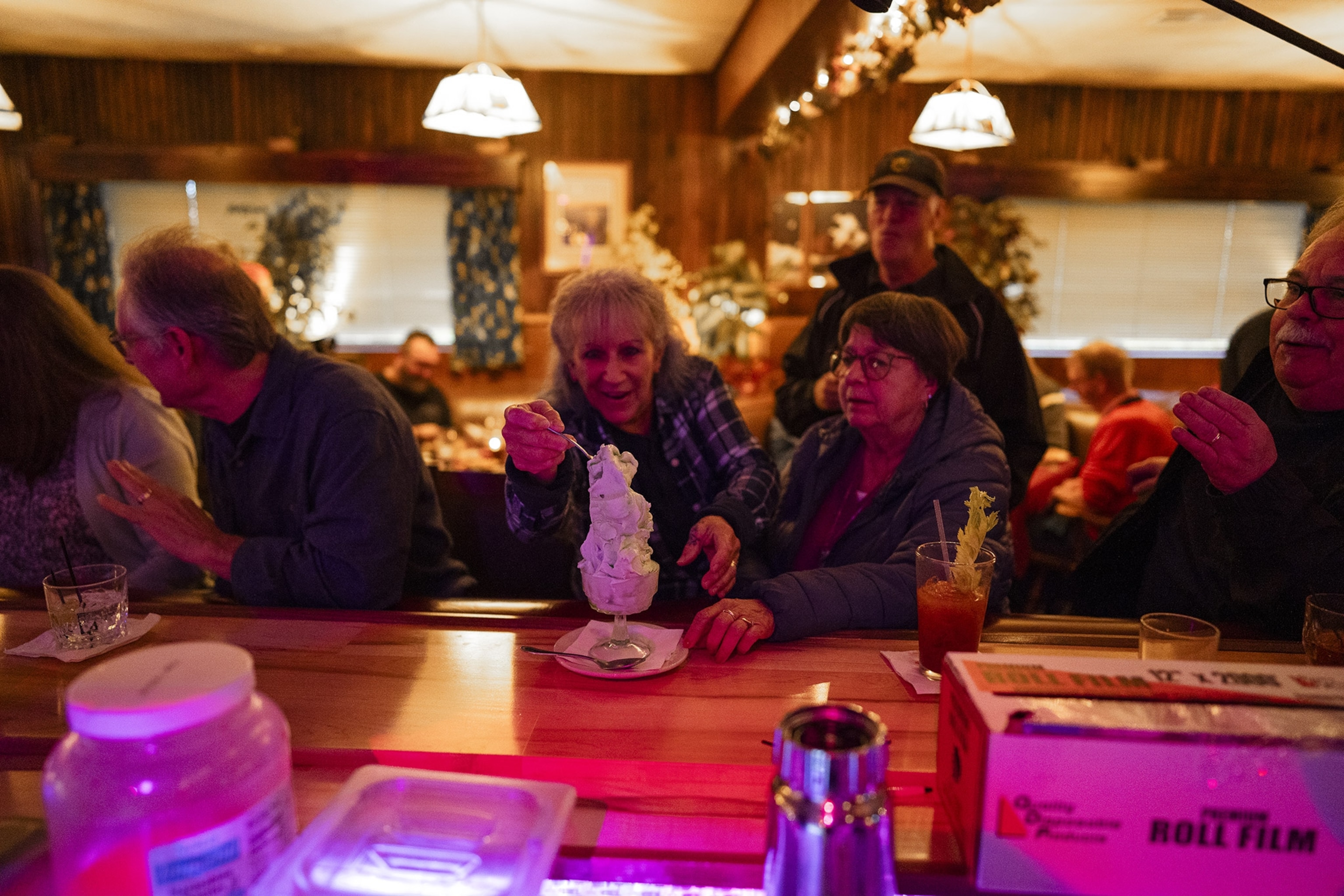 Four people sit at a dimly lit bar and share a tall ice cream sundae