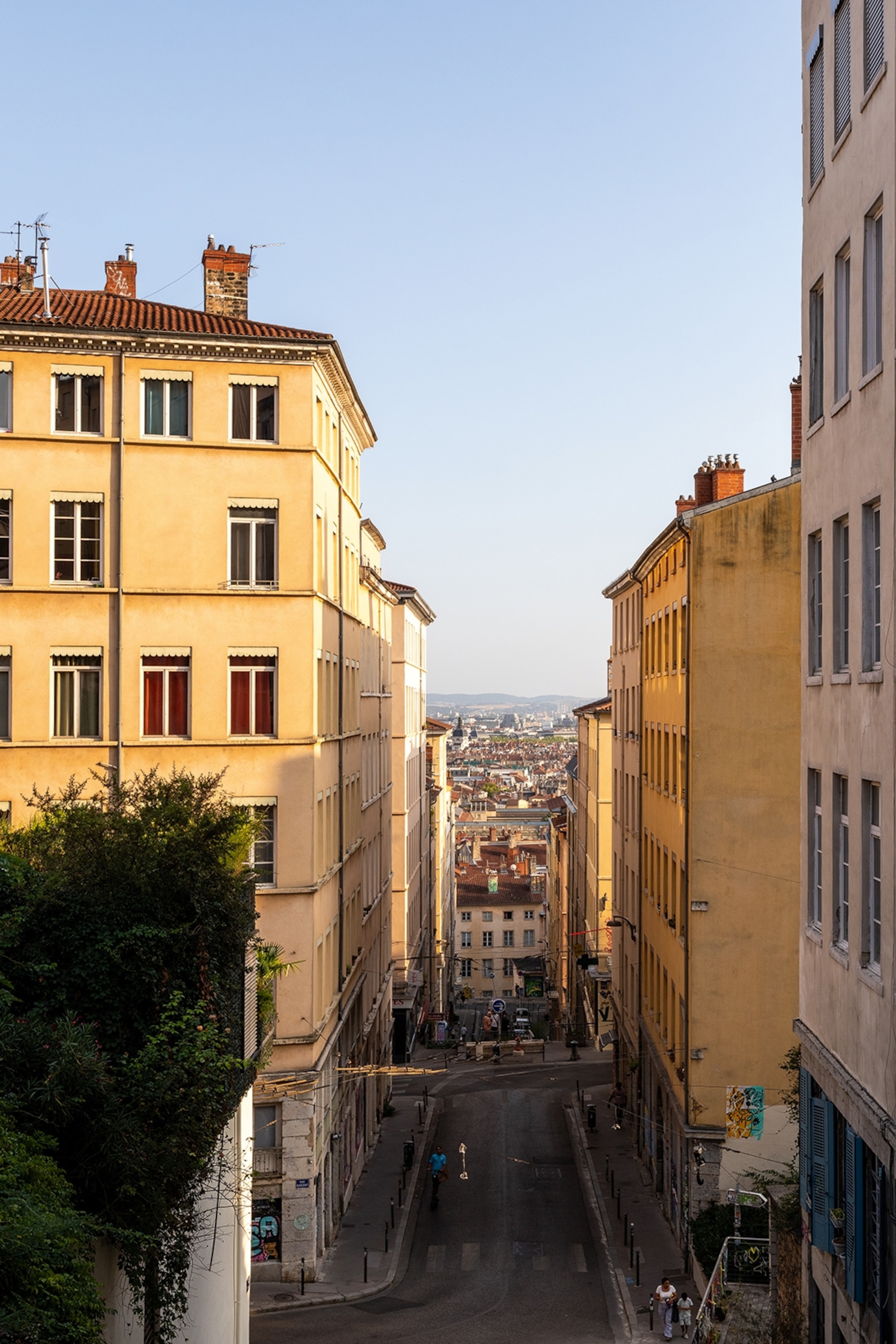 A city view down a hill with residential buildings on either side in the late afternoon sun.
