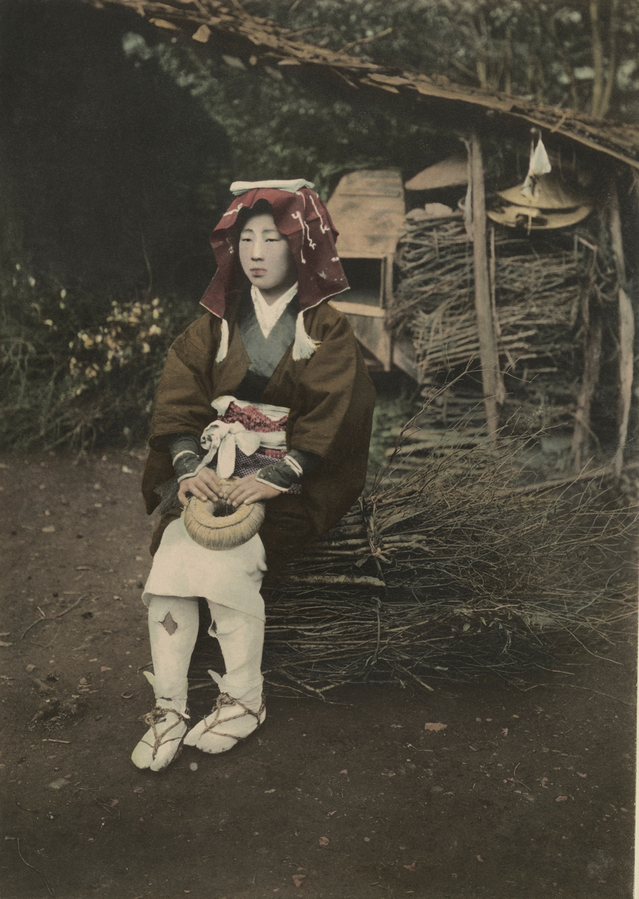 A farmer's daughter rests on her way to the city market. In her hands she holds the dougnut-style mat of straw which she uses as a pad when carrying her bundle on her head. This is not the every-day garb of the farm laborers; she is in her “Sunday best,” for her fuel must be peddled from house to house in town.