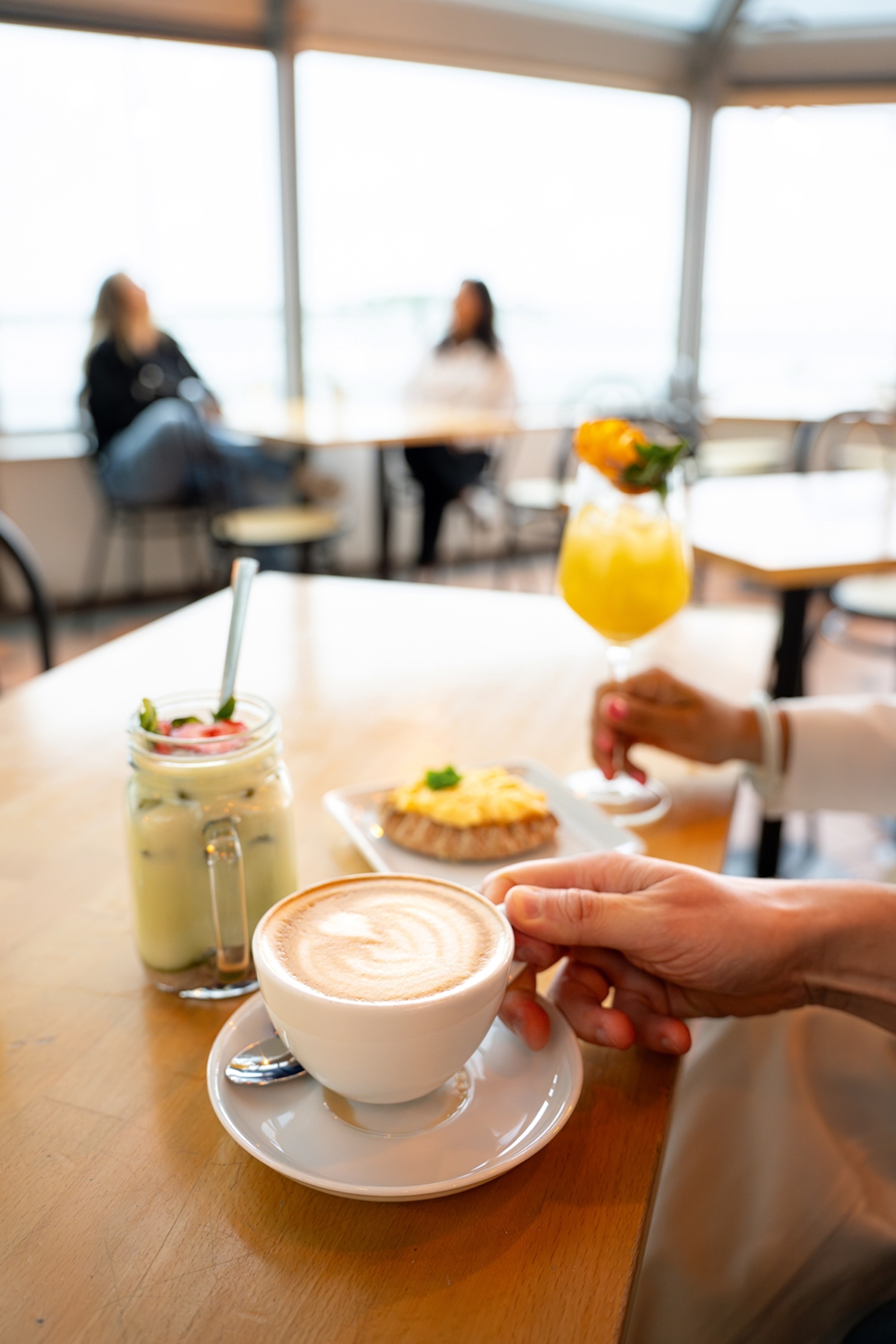 A close-up of a cafe counter with a selection of juices, a capucchino and a piece of pastry.