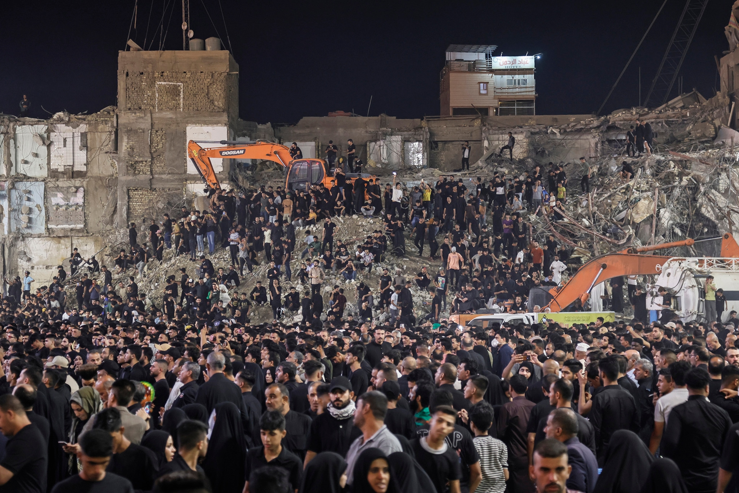 A group of people wearing black gather in the street in front of building demolition