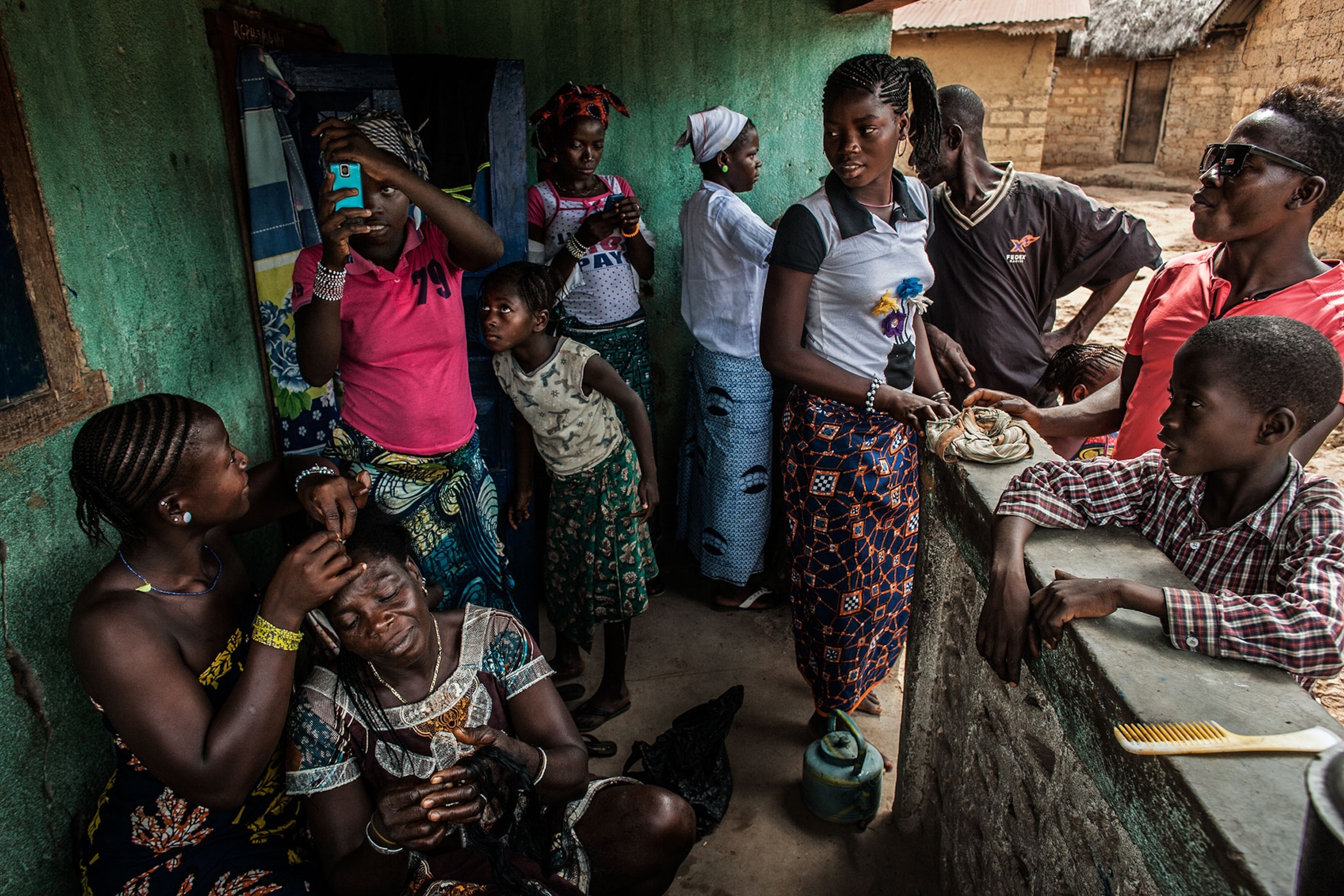 people congregating in a front porch area, braiding hair and talking