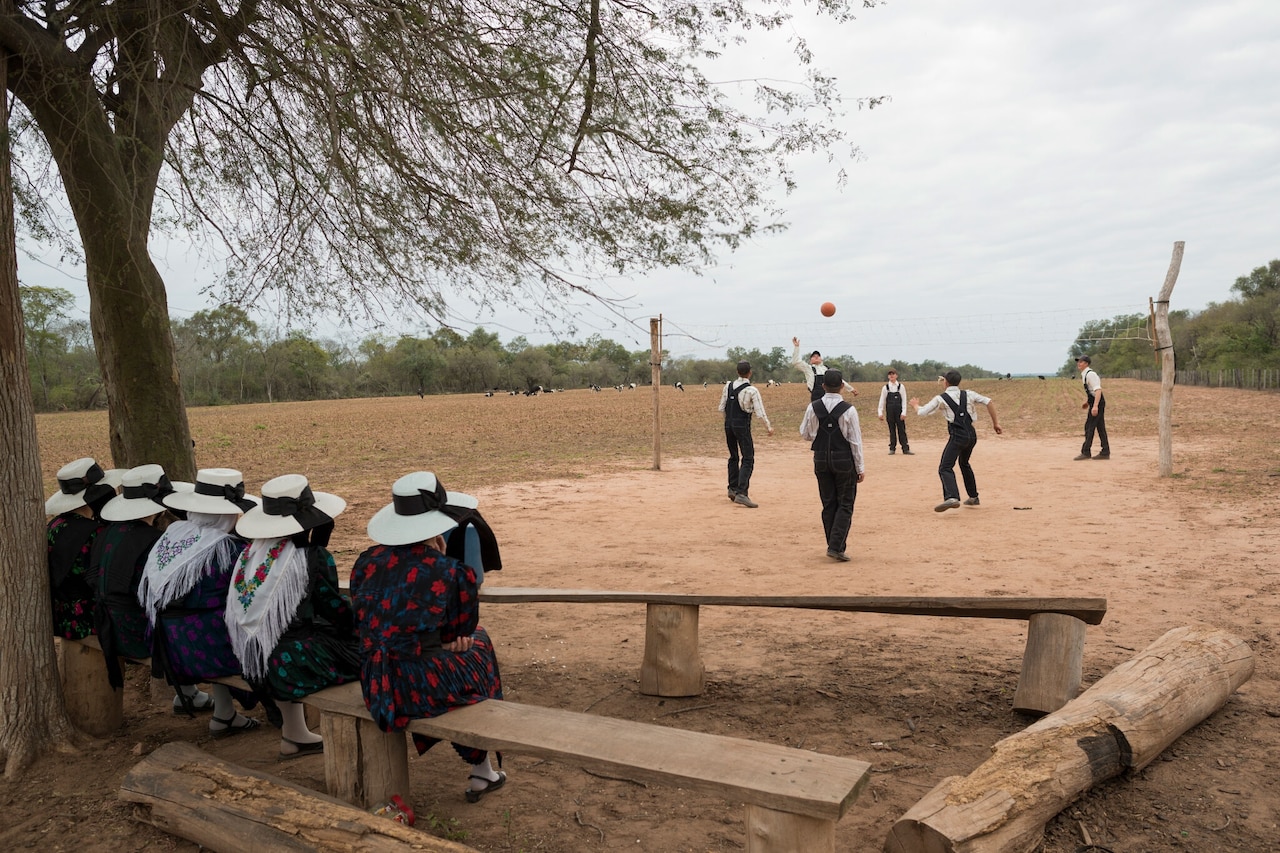 Los hombres jóvenes menonitas de entre 15 y 21 años juegan voleibol durante una salida dominical mientras las mujeres jóvenes los miran. Colonia El Palmar, Bolivia. 2013