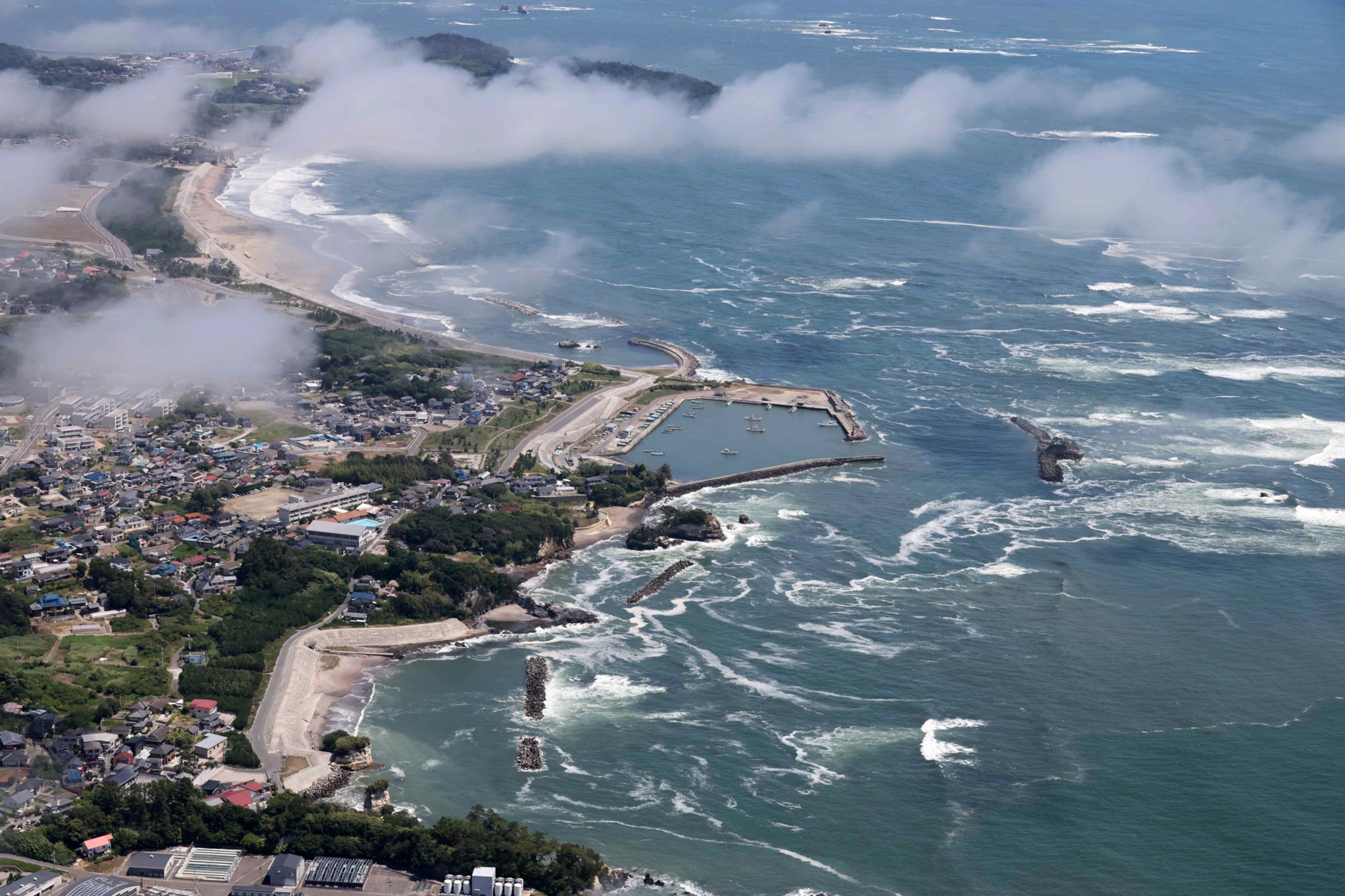 An aerial view of a coastline in Japan, where white-capped waves can be seen approaching the shore