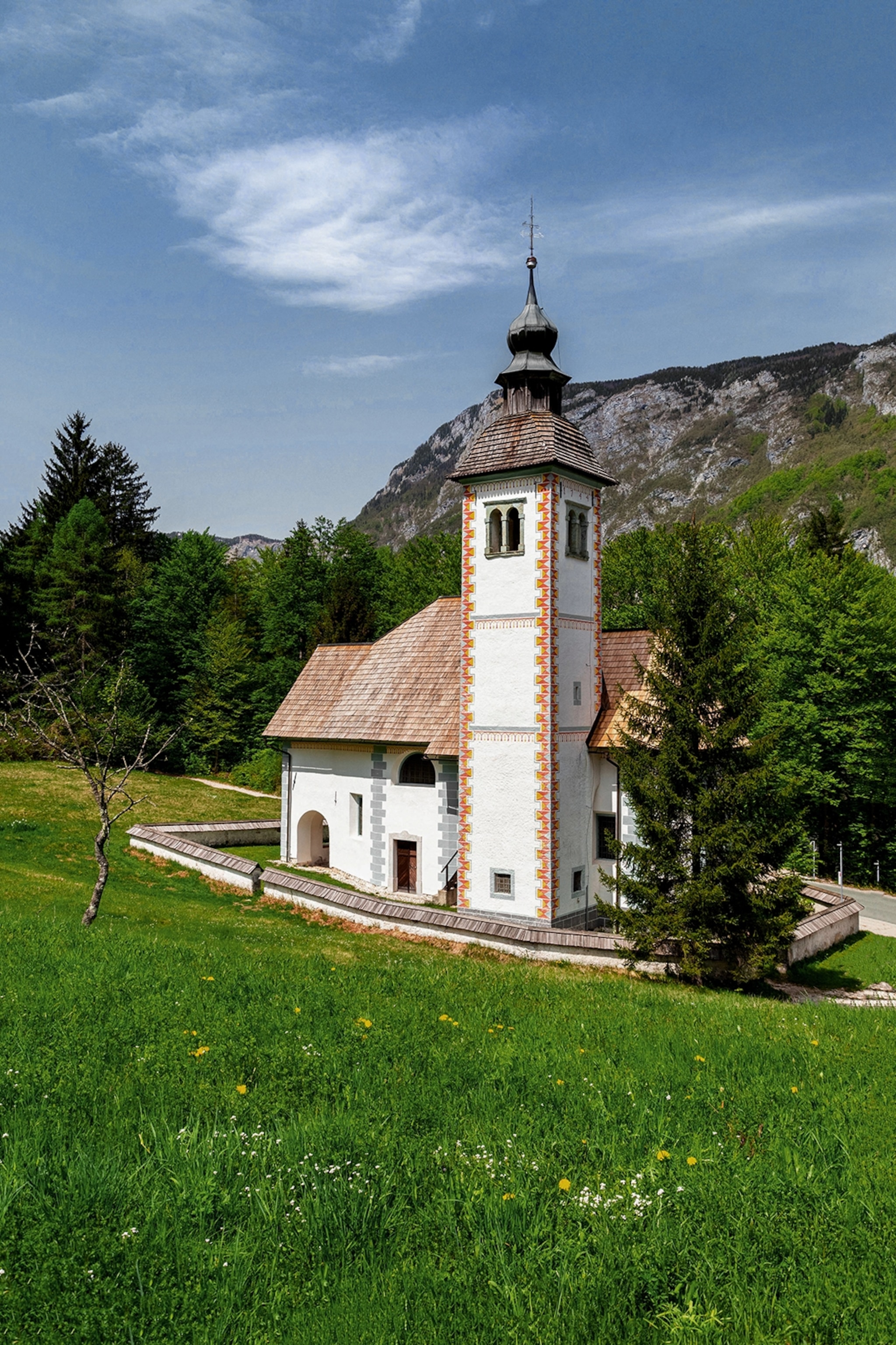 A small church on the grassy slope of a hill with trees in the back.