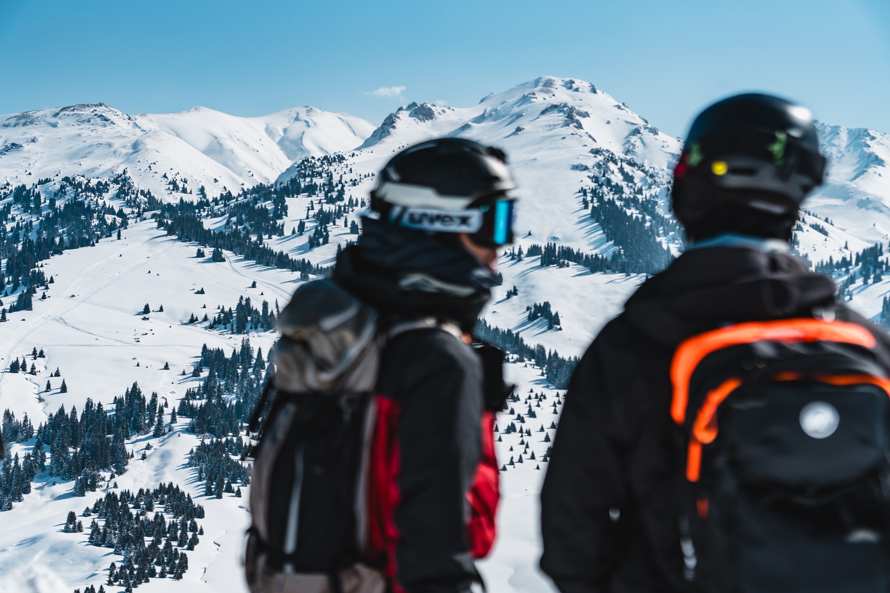 Two snowboarders discussing something with a snowy, mountain landscape in the back.