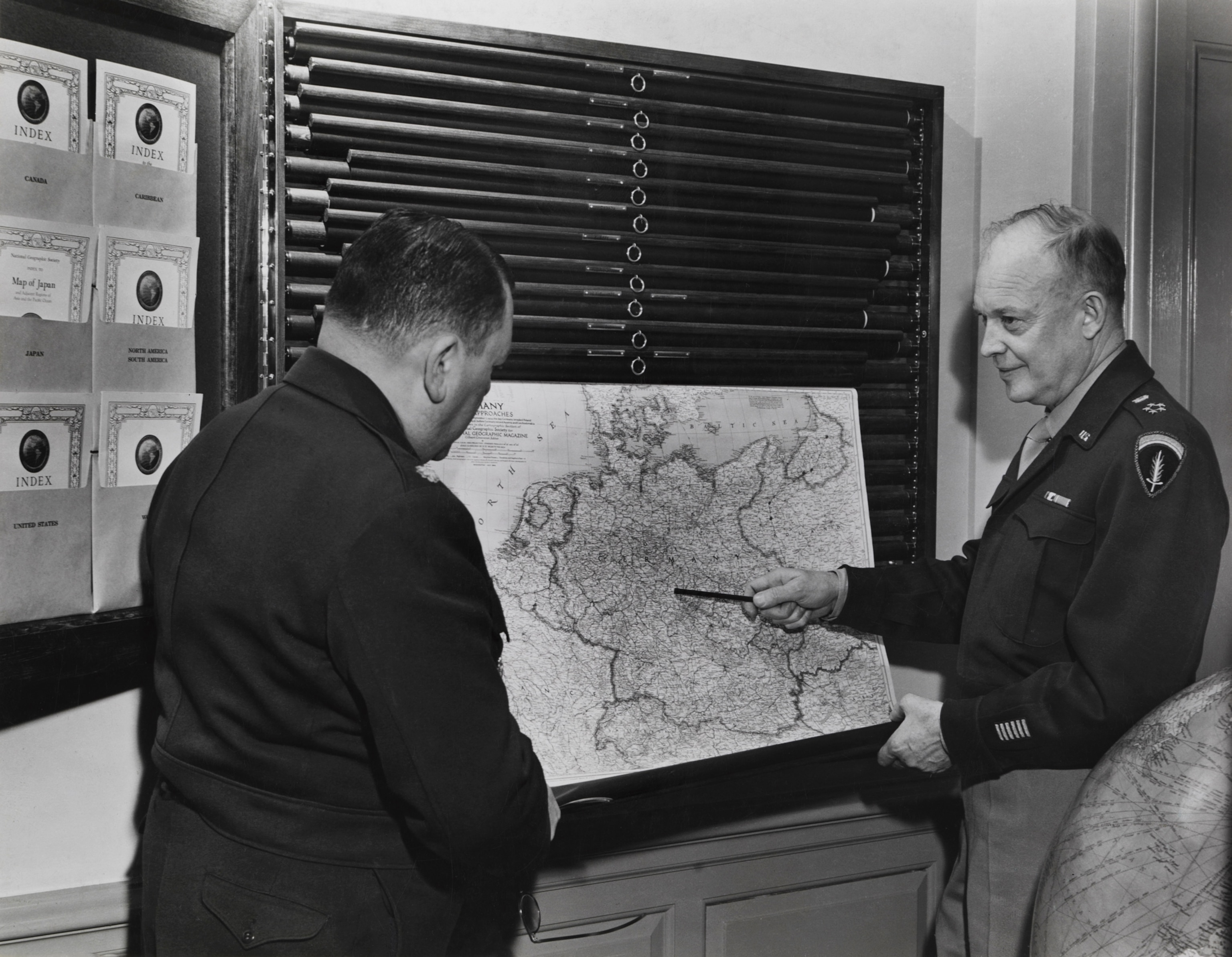 business A man stands pointing to a map that is hanging from a cabinet