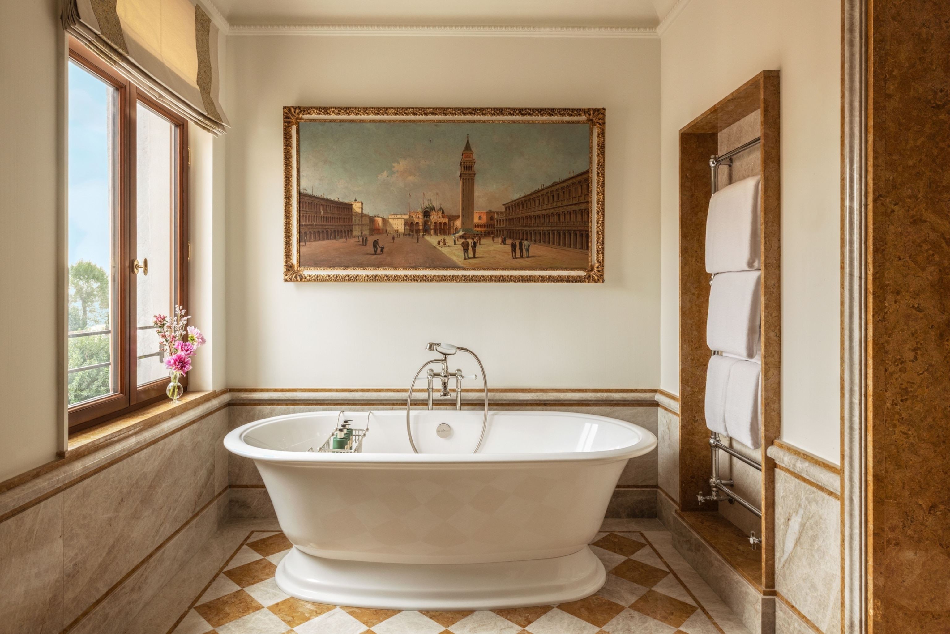 An elegant bathroom with a freestanding bathtub, marble finishes, folded towels, and a large framed painting above the tub.