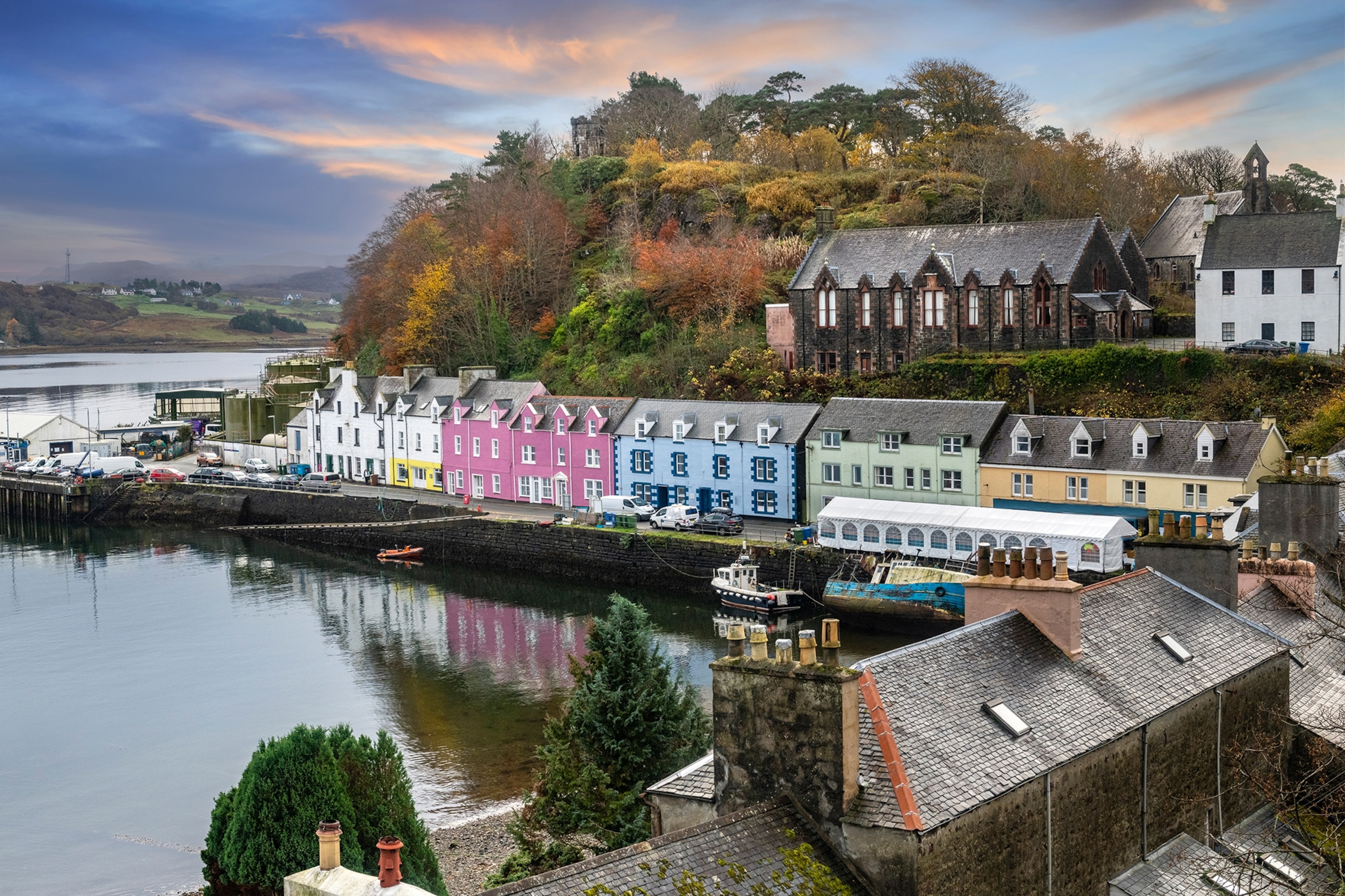 A wide view onto a small harbour with a handful of fishing boats and a row of colourful houses.