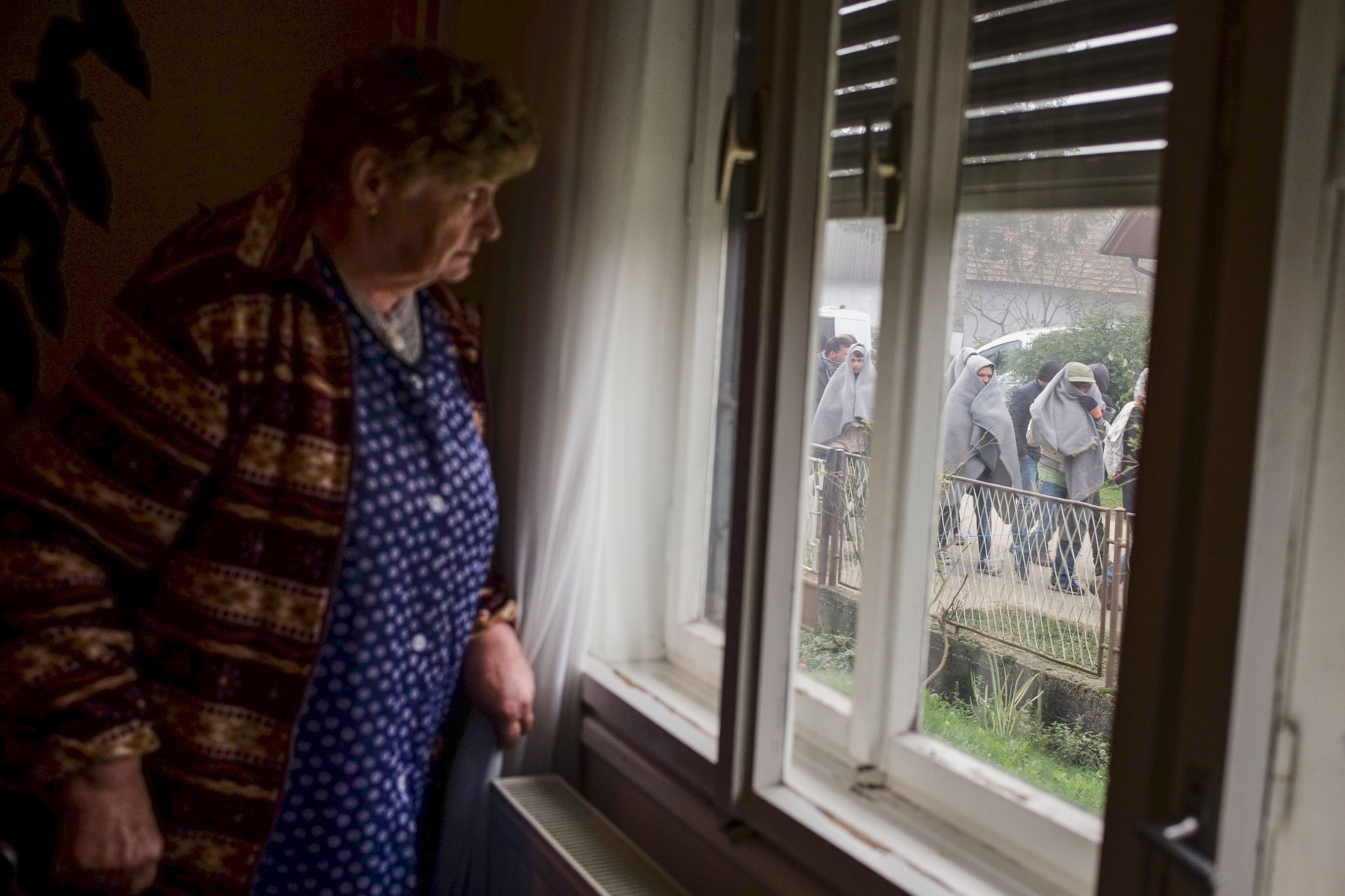 a local Slovenian woman watching refugees walk down the street