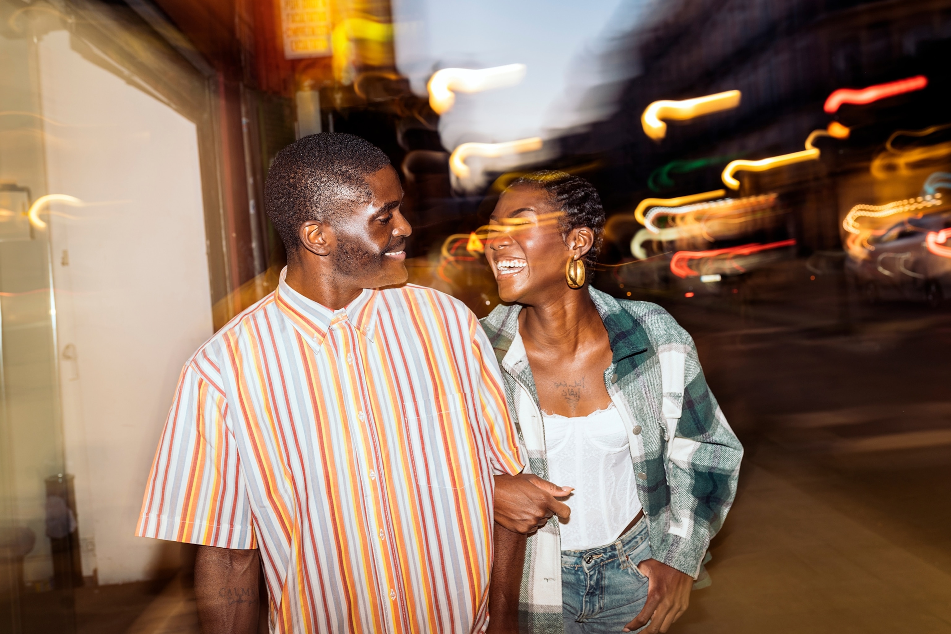A couple on a date shares a joyful moment while walking through a vibrant, illuminated street at night.