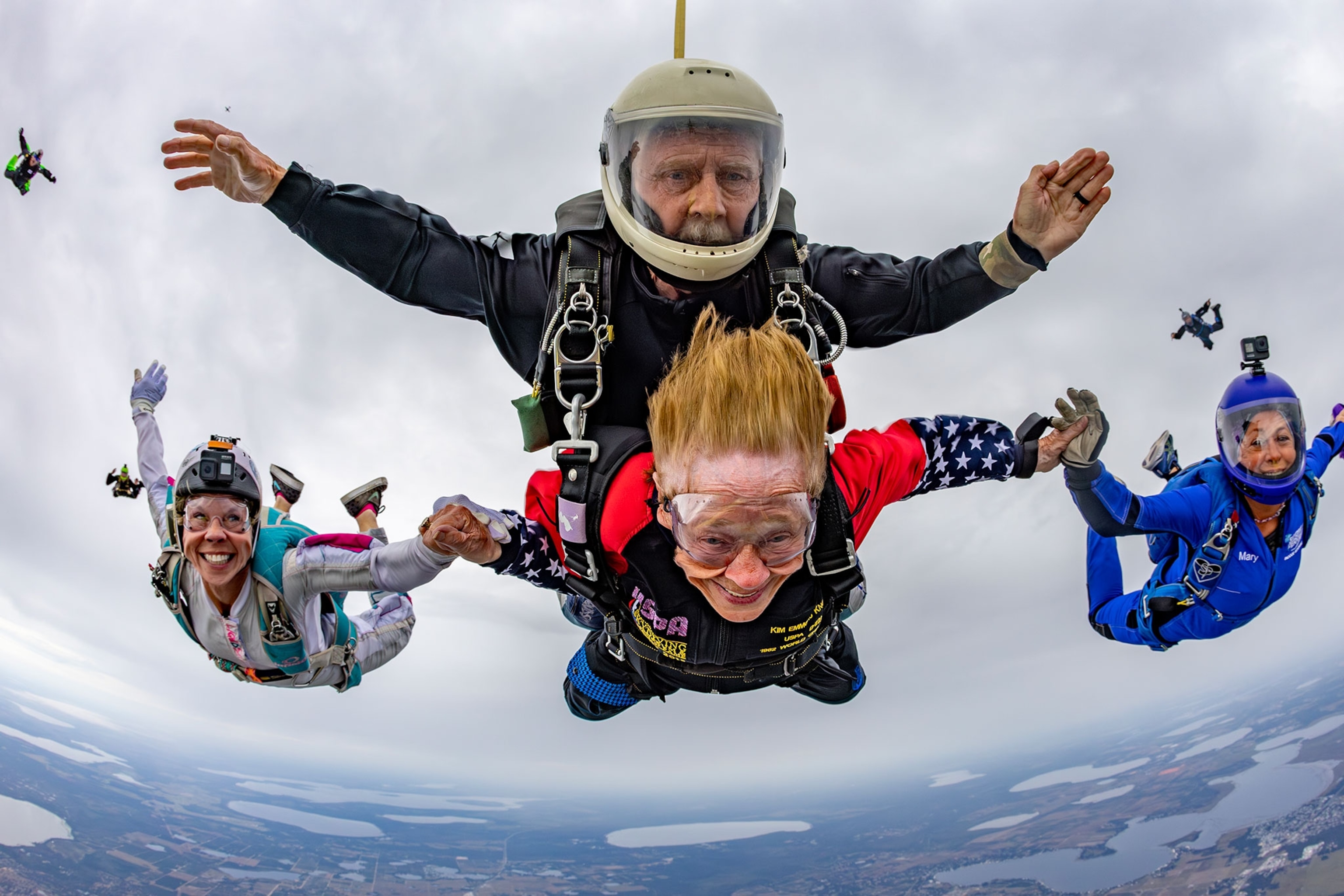 A womans hair is blowing in the wind with people encircling her and their bodies fly through the sky.