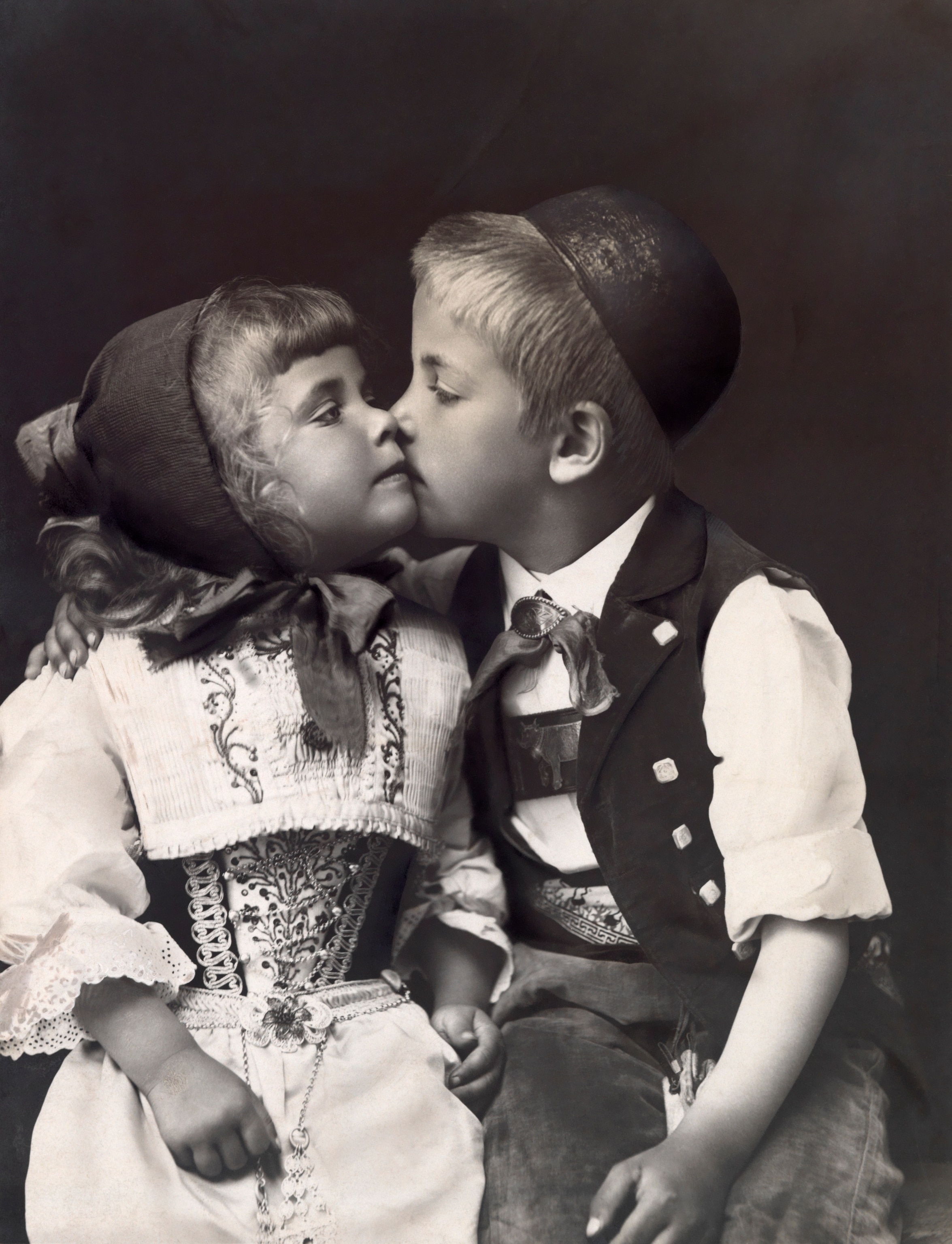 A young boy and girl in Swiss national costume share a kiss.