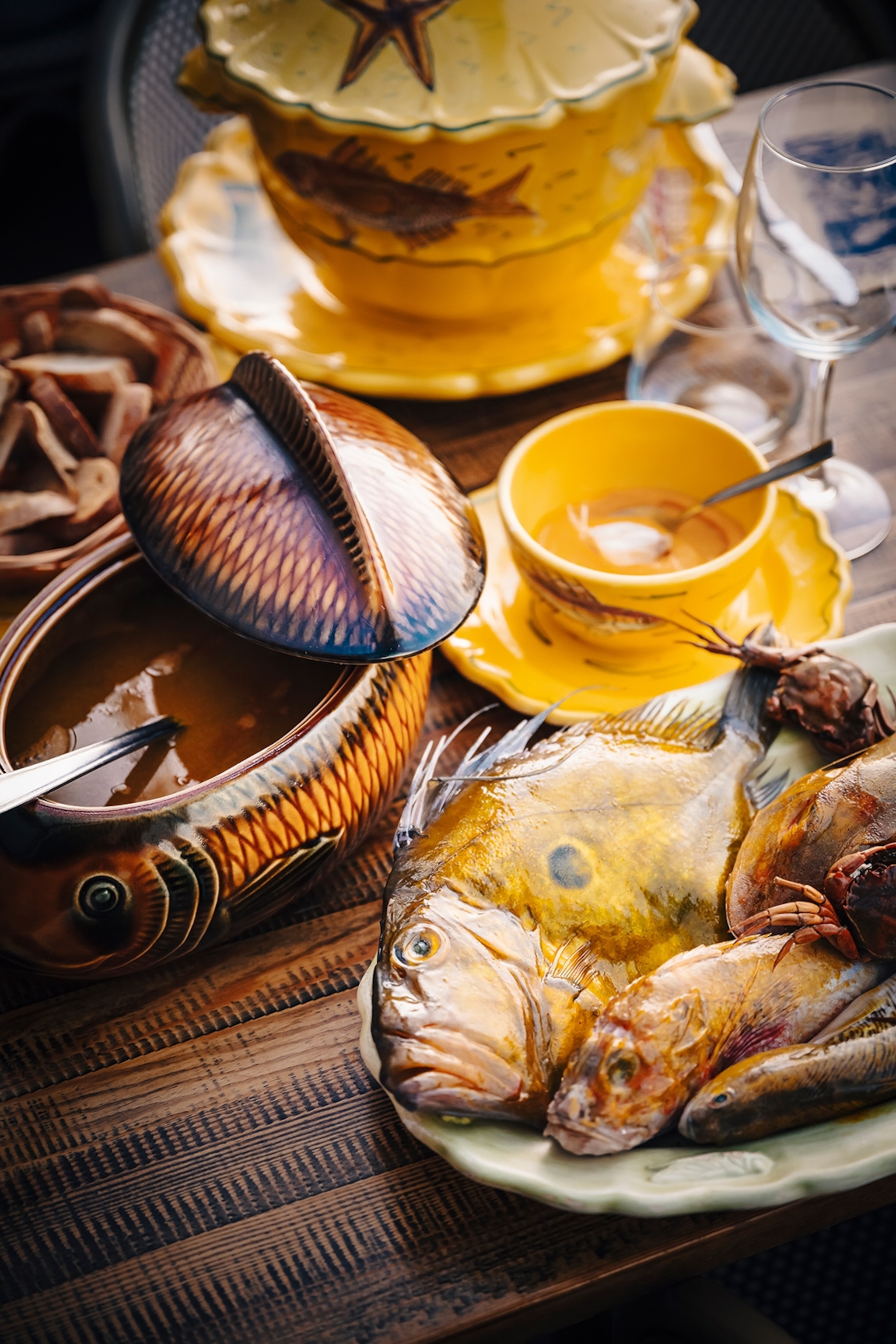 A decorated pot of fish soup with cooked fish on the side.
