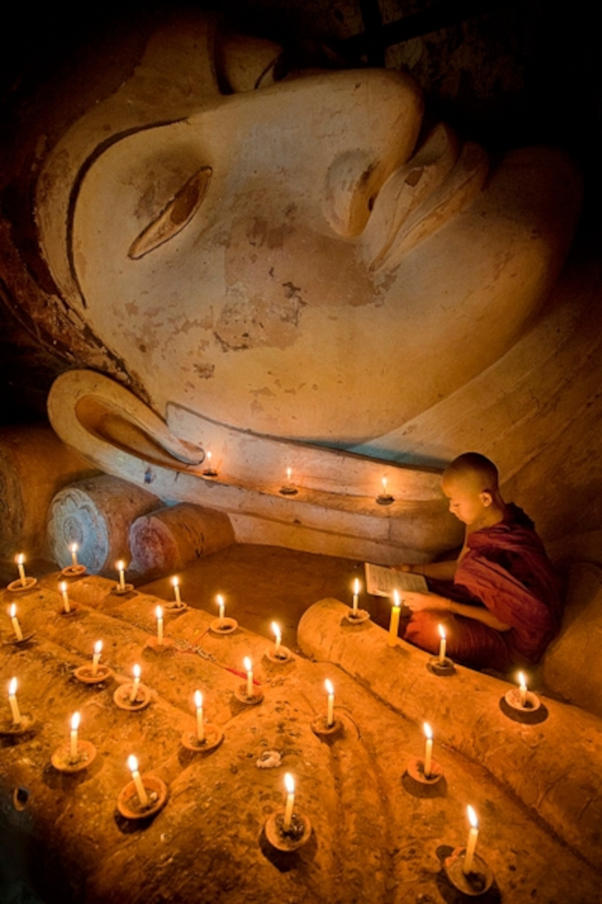 a young monk in Bagan, Myanmar, praying under the Buddha statue