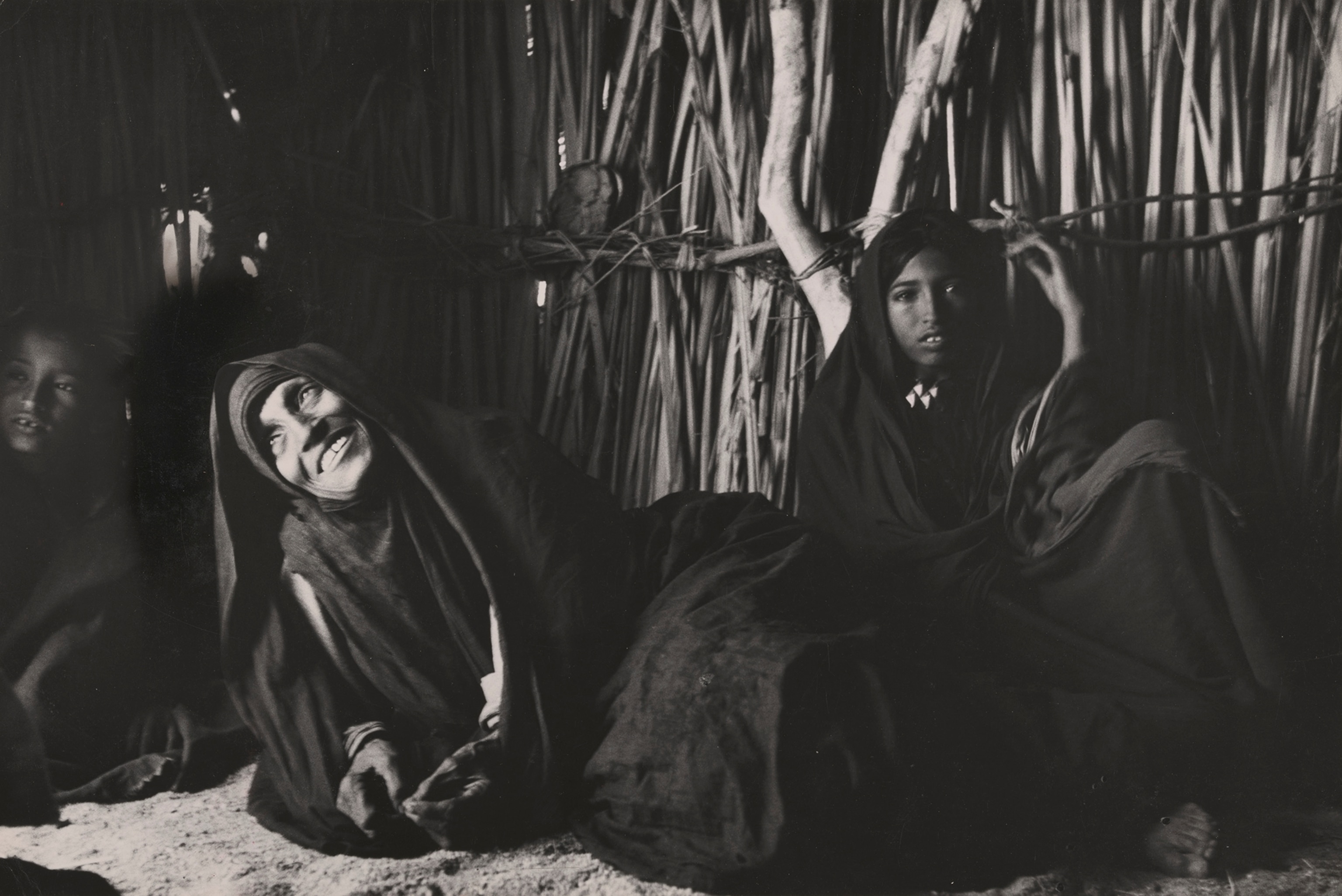 An elderly widow wearing a robe as a hood lays smiling in front of her granddaughter