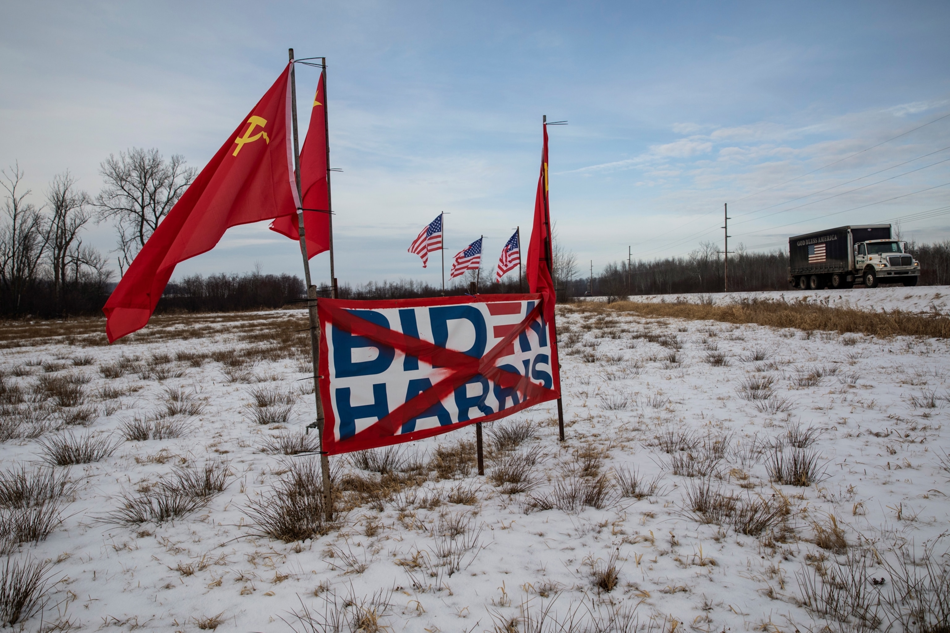 A sign for Joe Biden and Kamala Harris with red communist flags stands in a snowy farm field