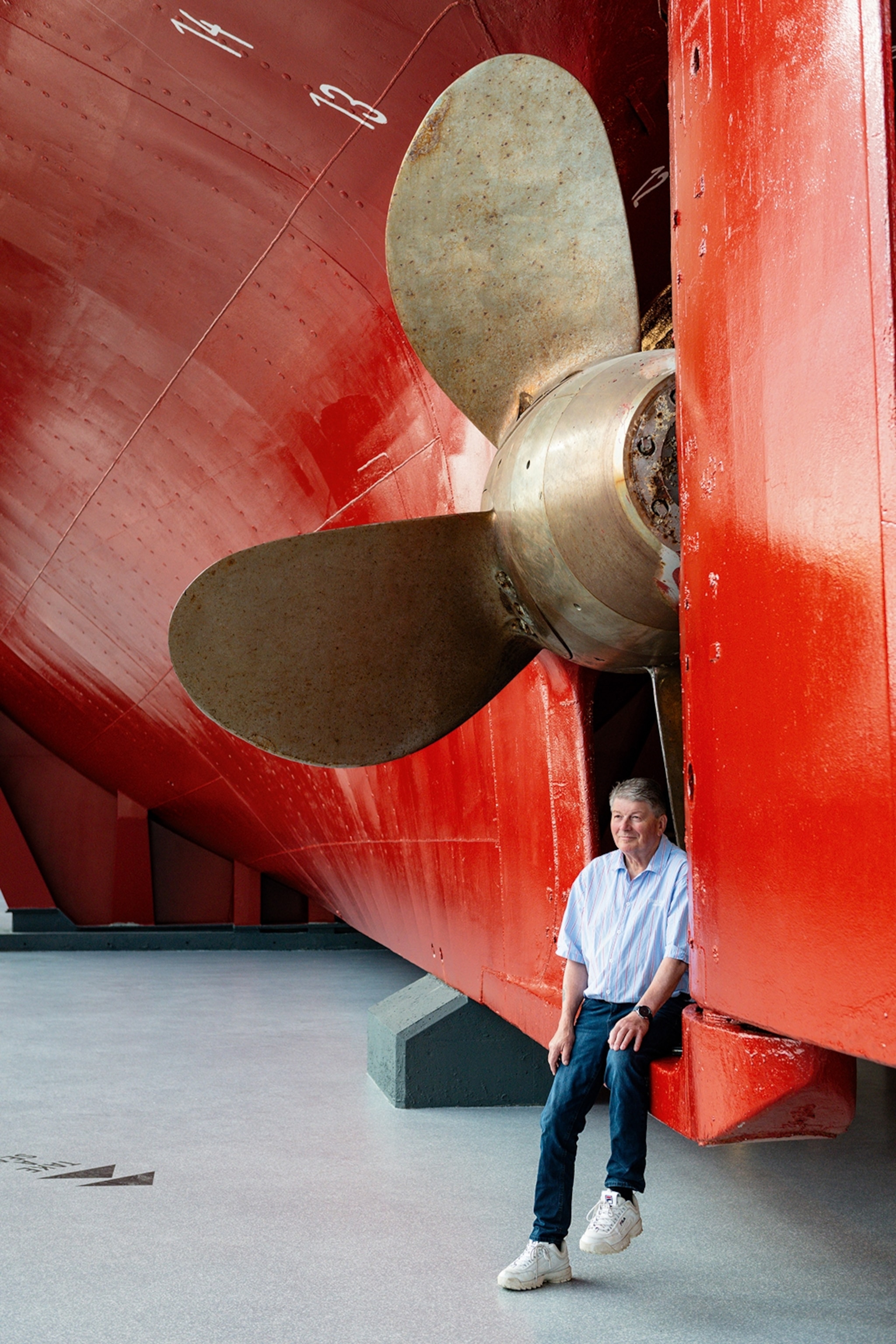 A man leaning against the lower propeller of a gigantic steel boat.