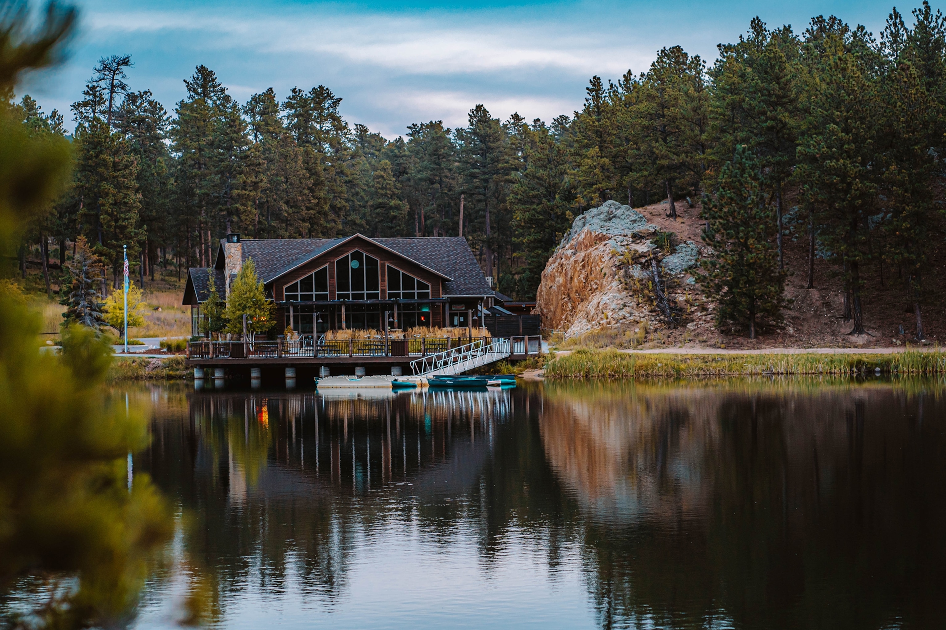 A lodge sits on the edge of a calm, black lake, in front of a small dock.