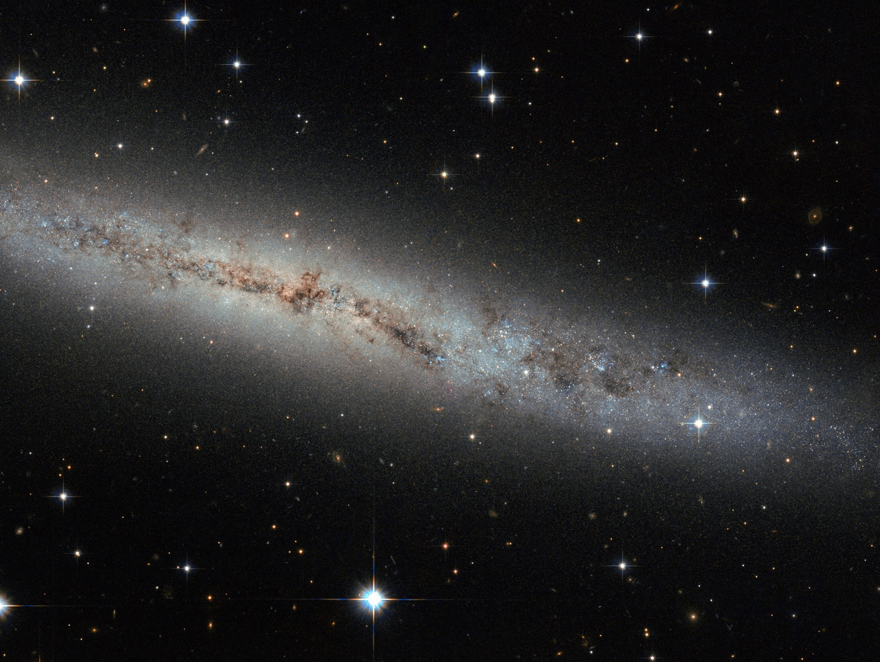 This new Hubble image shows spiral galaxy ESO 373-8. Together with at least seven of its galactic neighbours, this galaxy is a member of the NGC 2997 group. We see it side-on as a thin, glittering streak across the sky, with all its contents neatly aligned in the same plane.