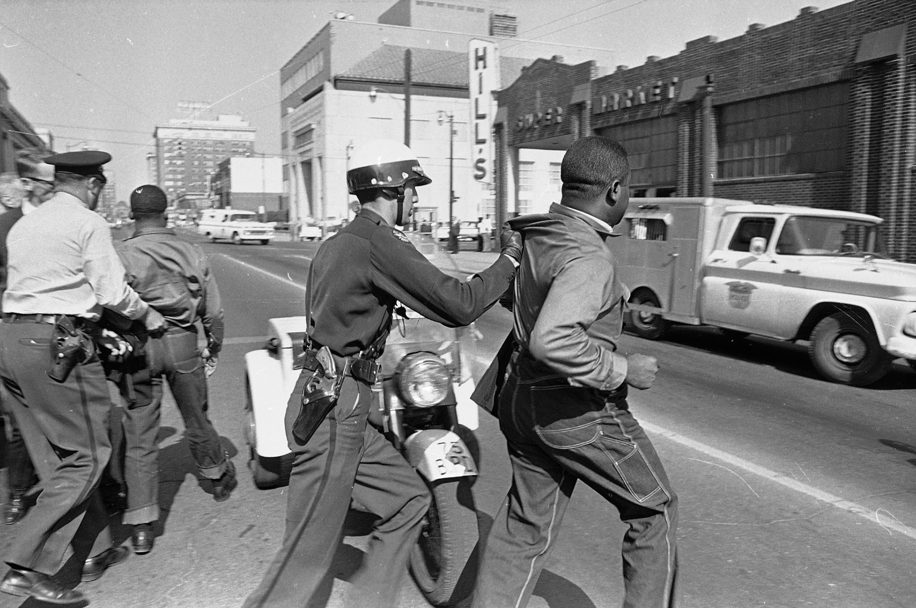 Police officers push two men towards a vehicle.