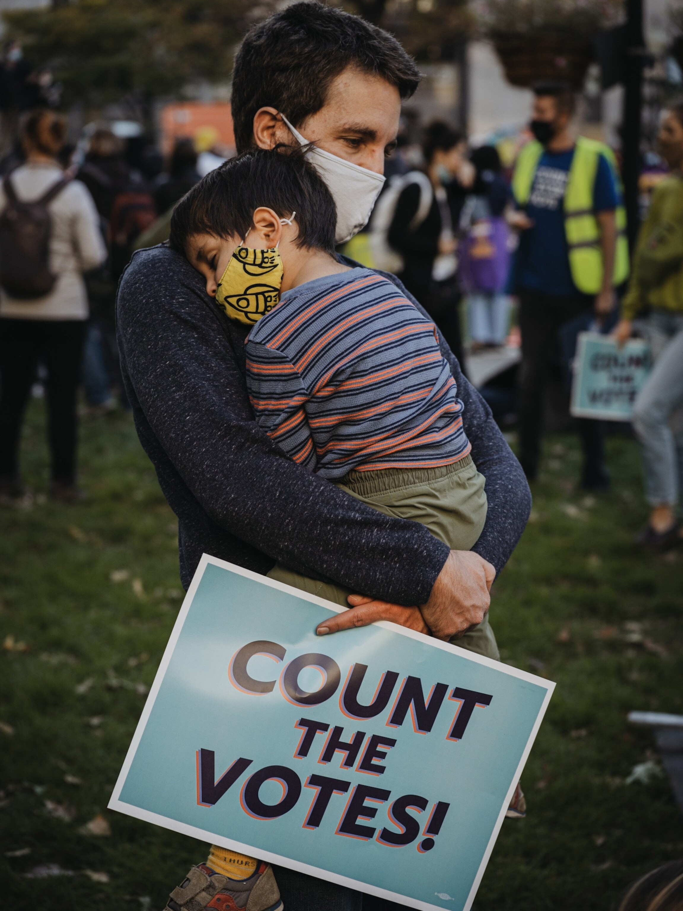 Man holding his child in his arms with a sign reading "count the votes"