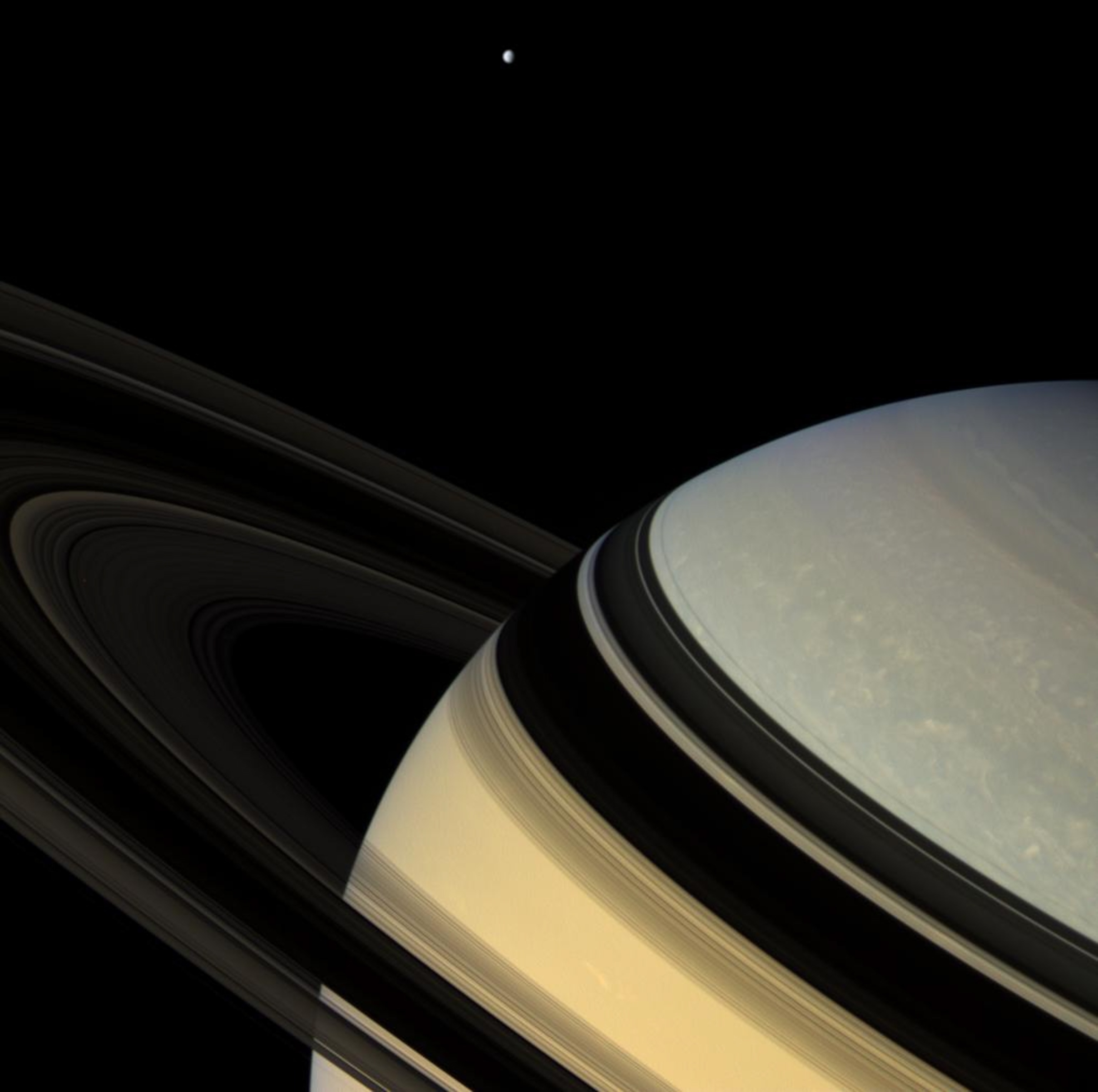 Magnificent blue and gold Saturn floats obliquely as one of its gravity-bound companions, Dione, hangs in the distance.