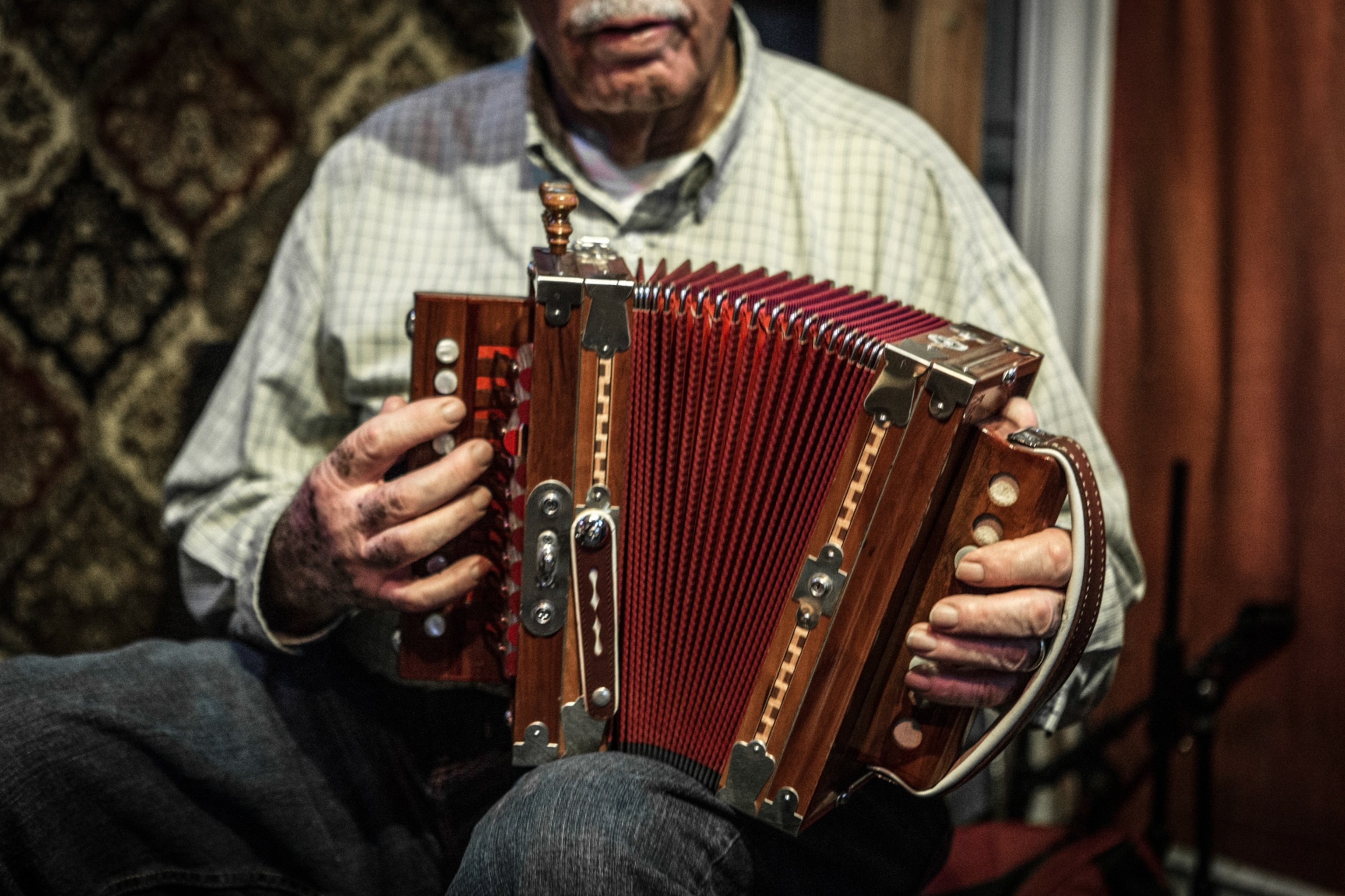 An elderly person plays a red and wooden accordion with focus on their hands.