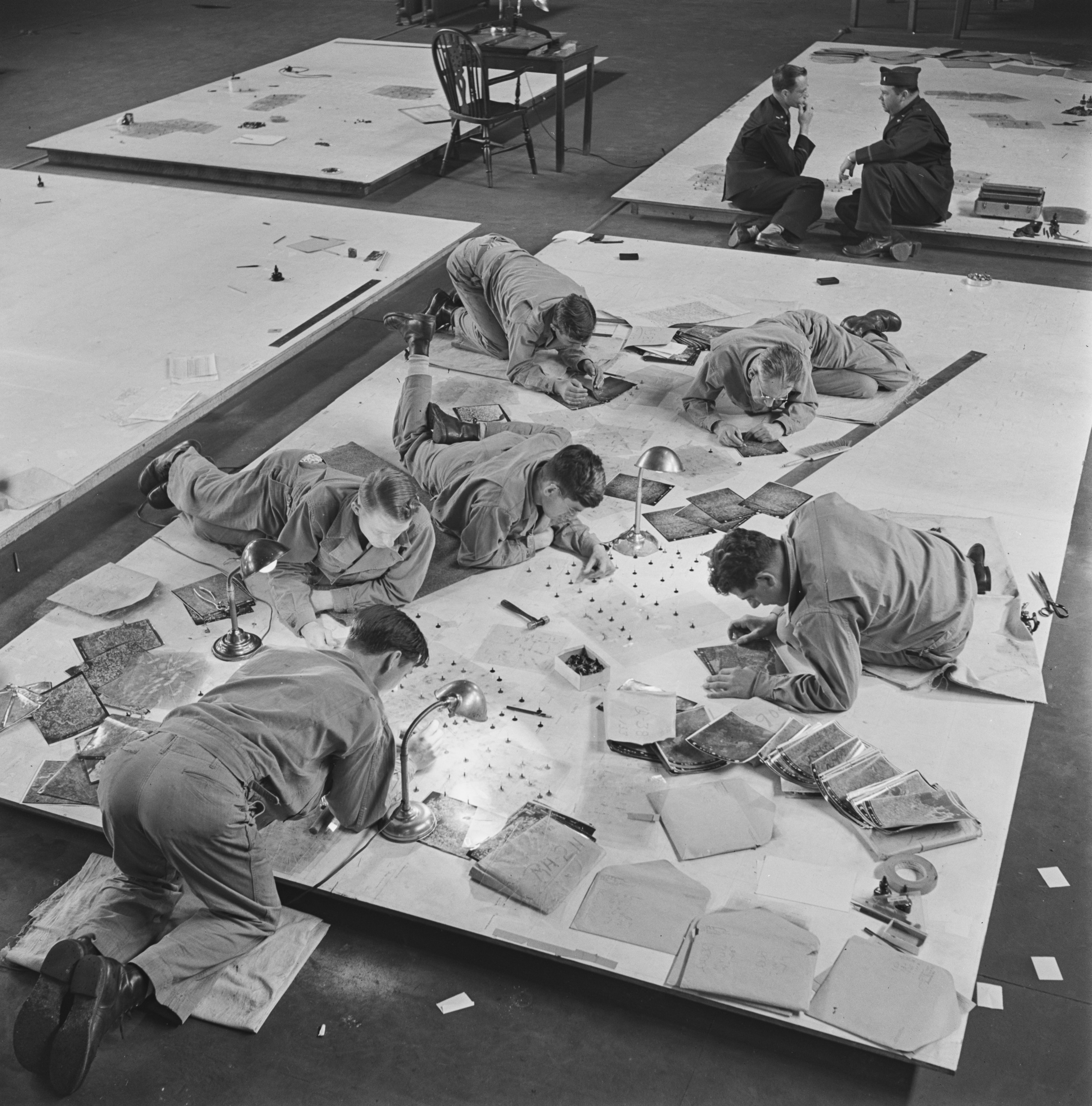 United States Army Air Forces (USAAF) staff from a Photographic Reconnaissance Unit lay out photographs on a slotted template board to locate control points of visible landmarks in enemy territory.