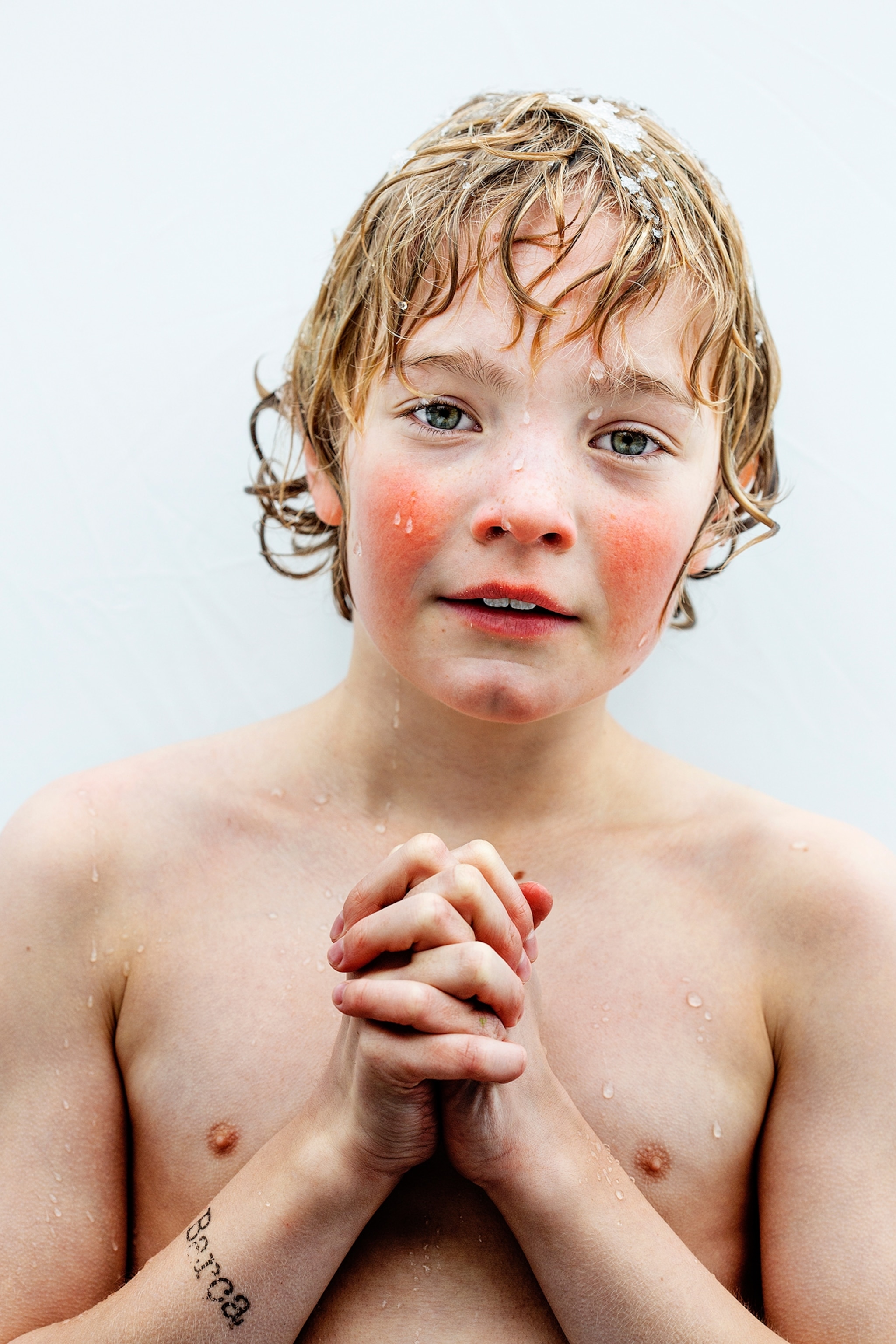 boy with wet hair and rosy cheeks clasping his hands together.