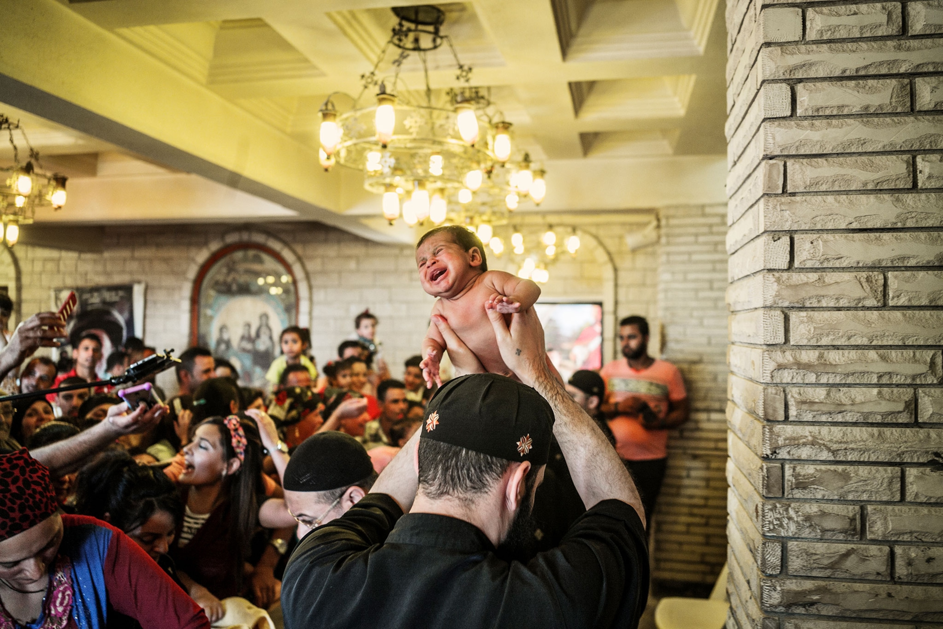 a priest takes a baby to be baptized at the Jebel El-Tier Moulid