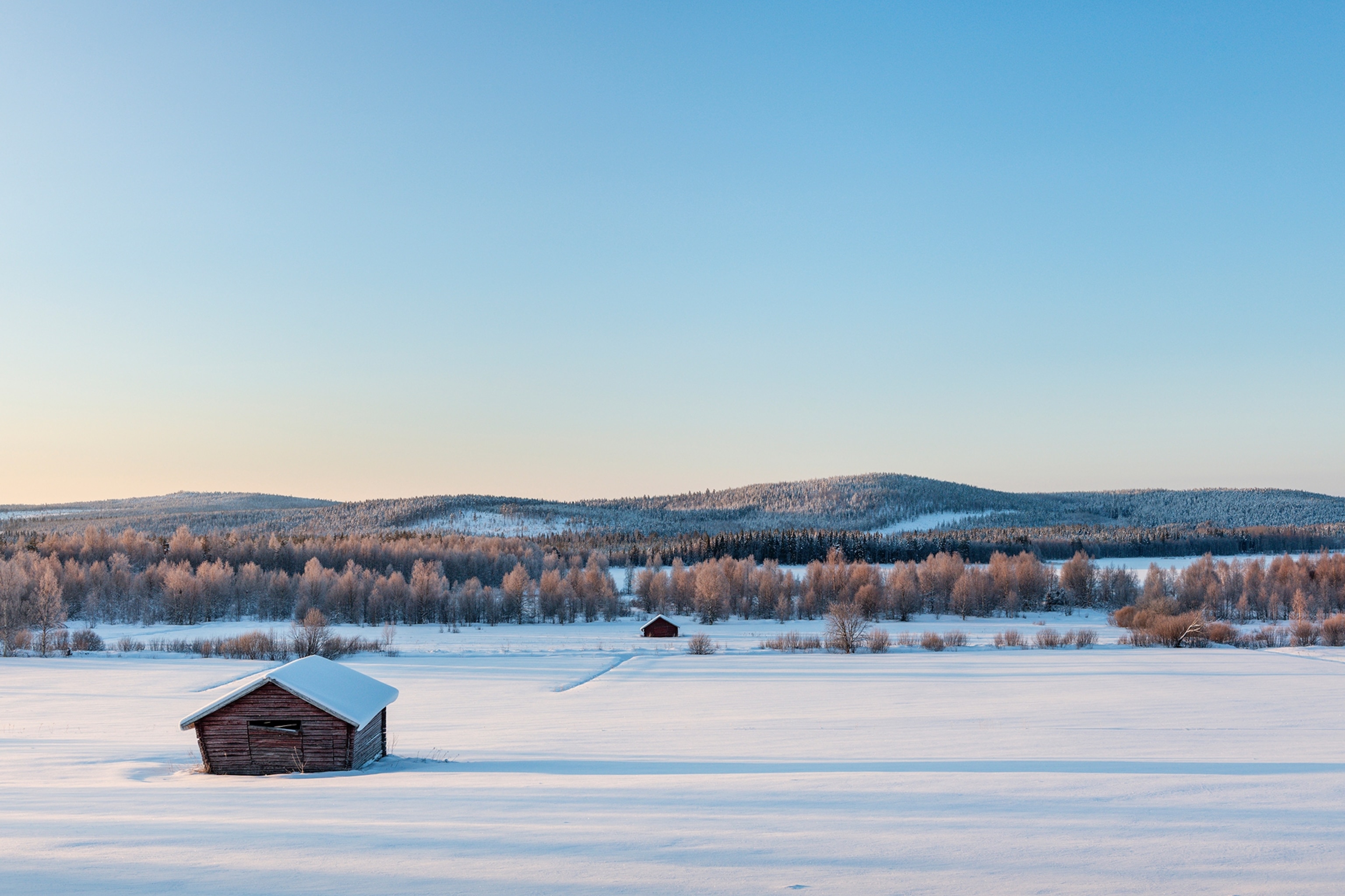 A frozen frozen river hidden beneath snow, with forested hills in the background.